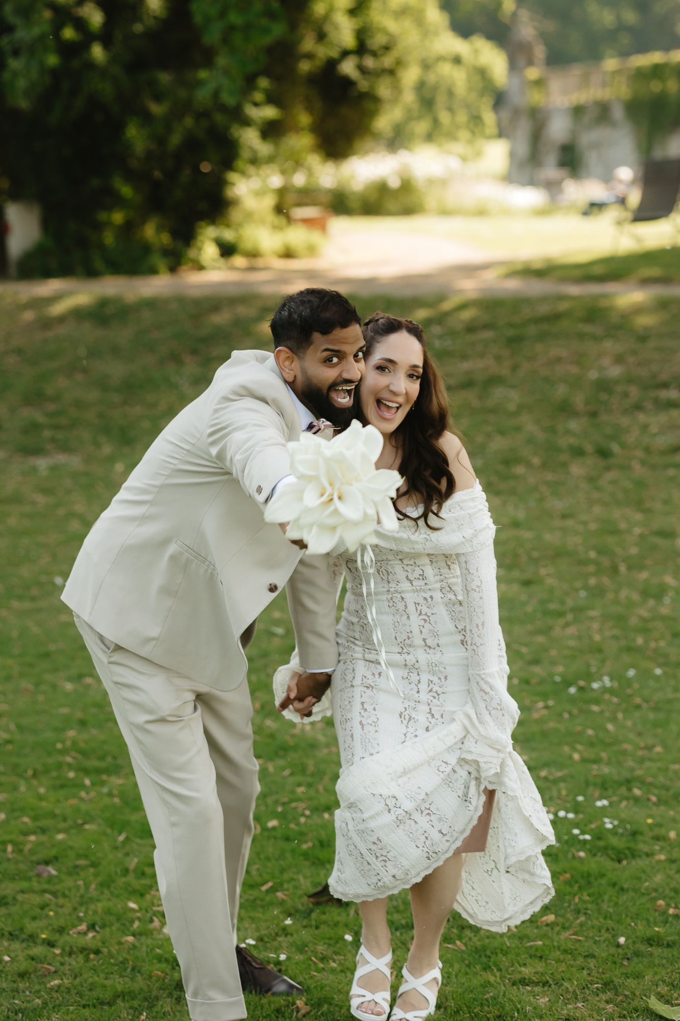 Joyful couple in white attire playing and laughing together on a sunny lawn.