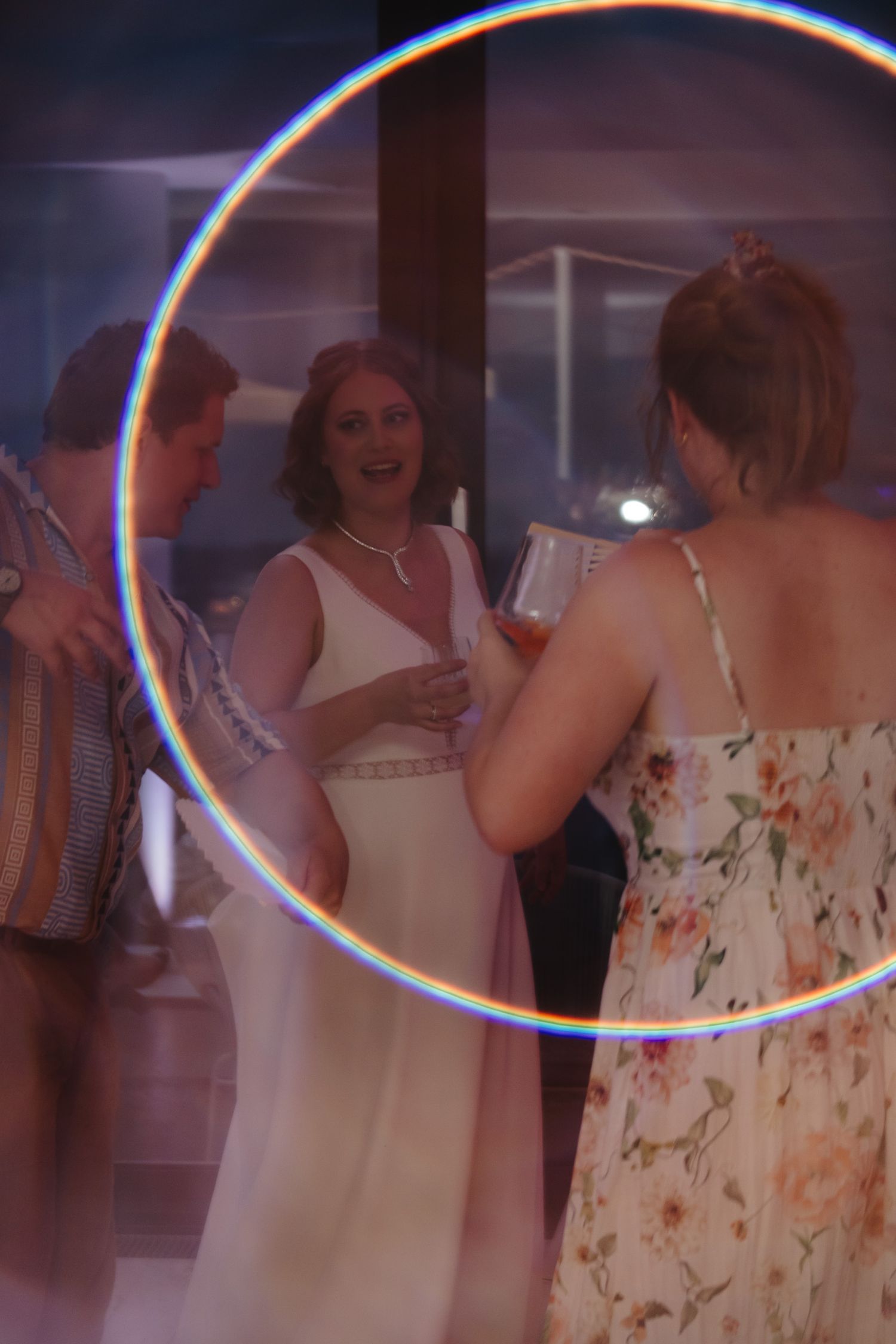 People in formal attire gather and socialize at an evening event with a circular light effect in the frame.