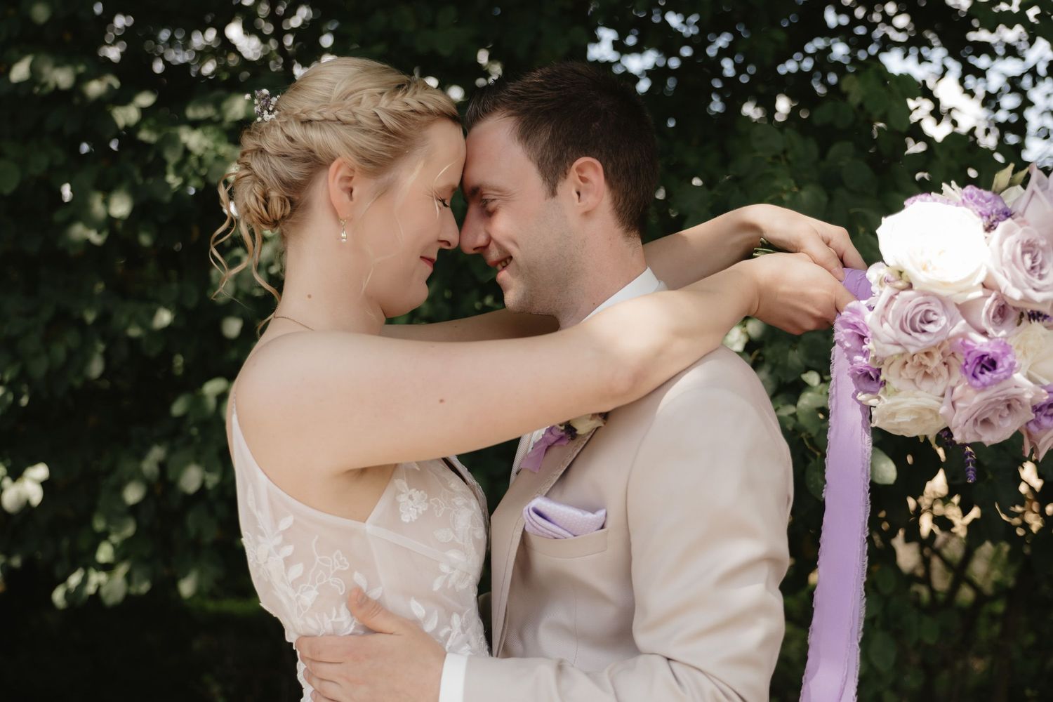 A romantic couple embraces during their wedding ceremony in a lush outdoor garden setting.