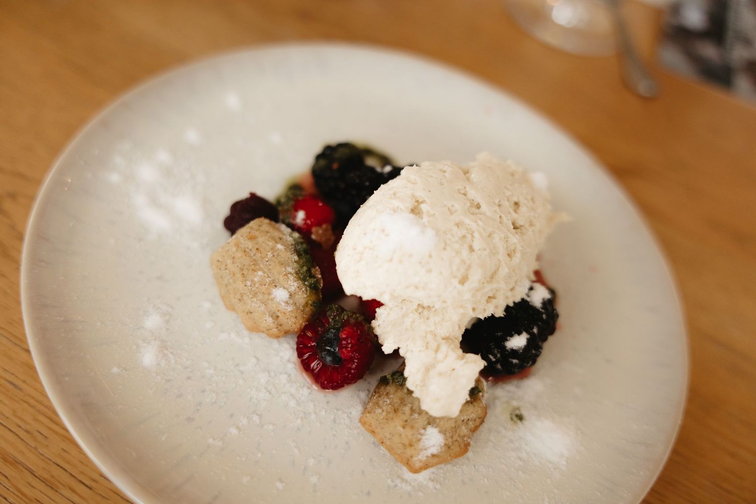 A dessert plate with vanilla ice cream, fresh berries, and cookie crumbles on a wooden table.