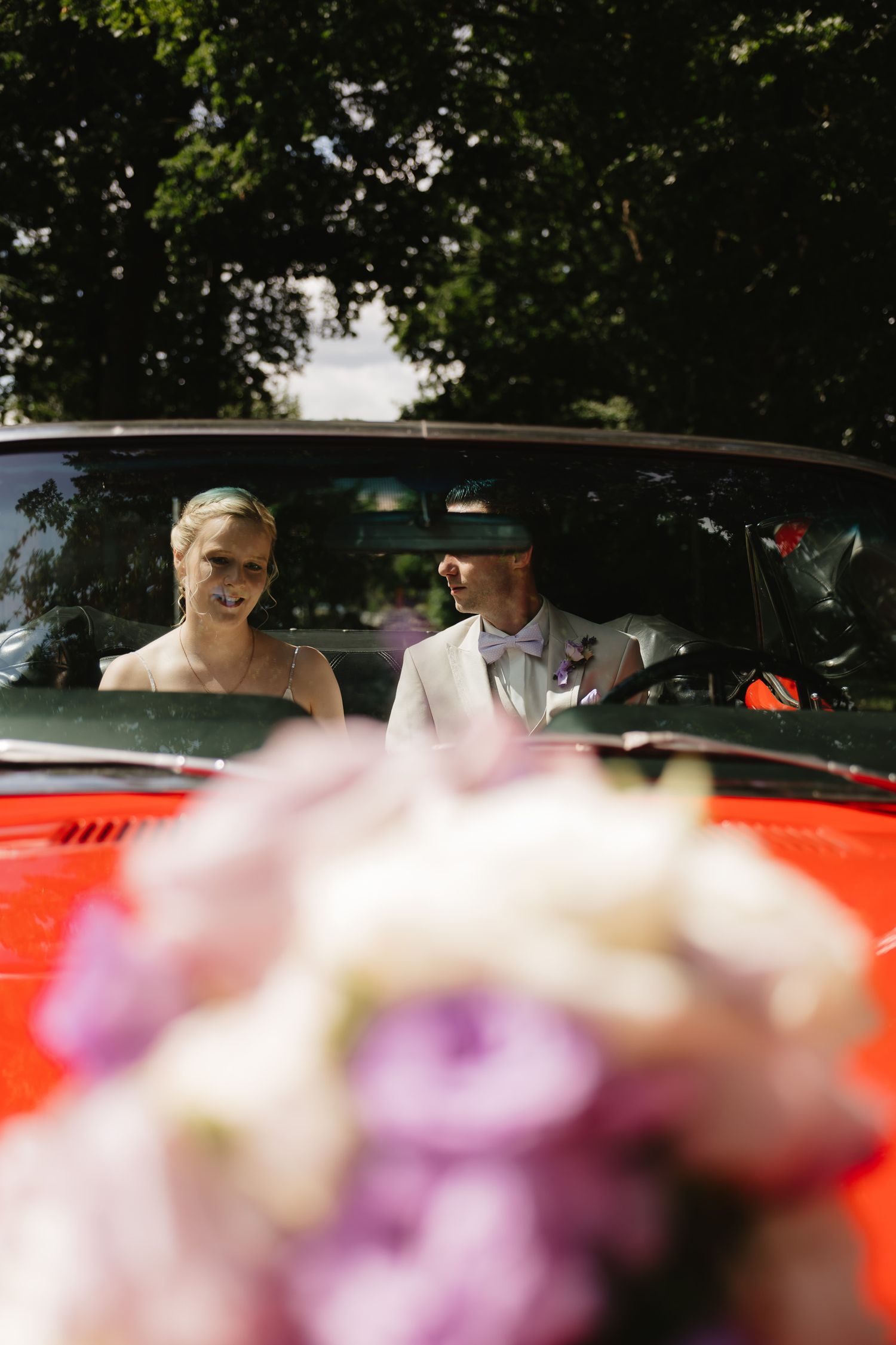 A red vintage car with colorful flowers in the foreground during a wedding celebration.