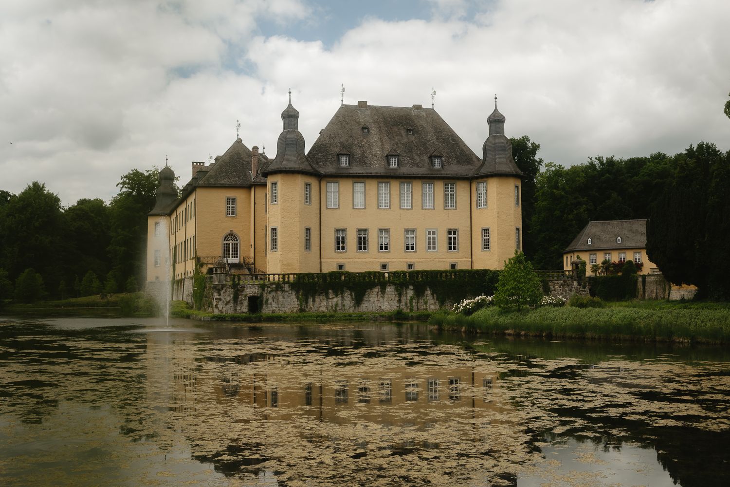 Panoramic view of a grand chateau with a reflective lily pond in the foreground.