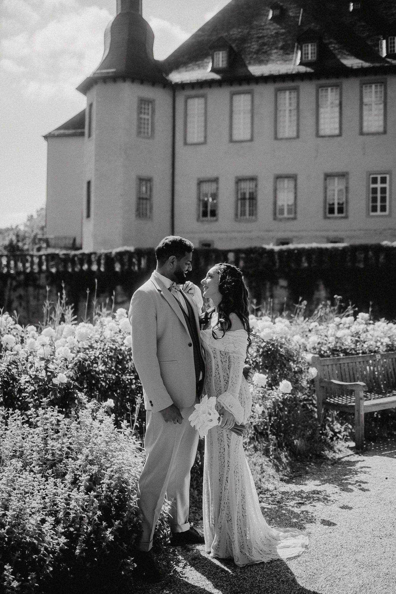 Black and white wedding portrait in front of historic building with garden landscape.
