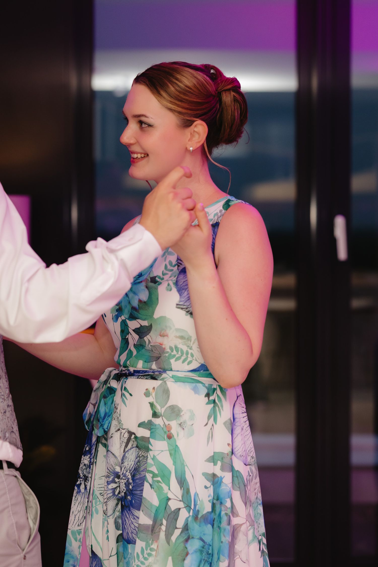 A person in a floral print dress with turquoise and white colors smiles during what appears to be a formal event.