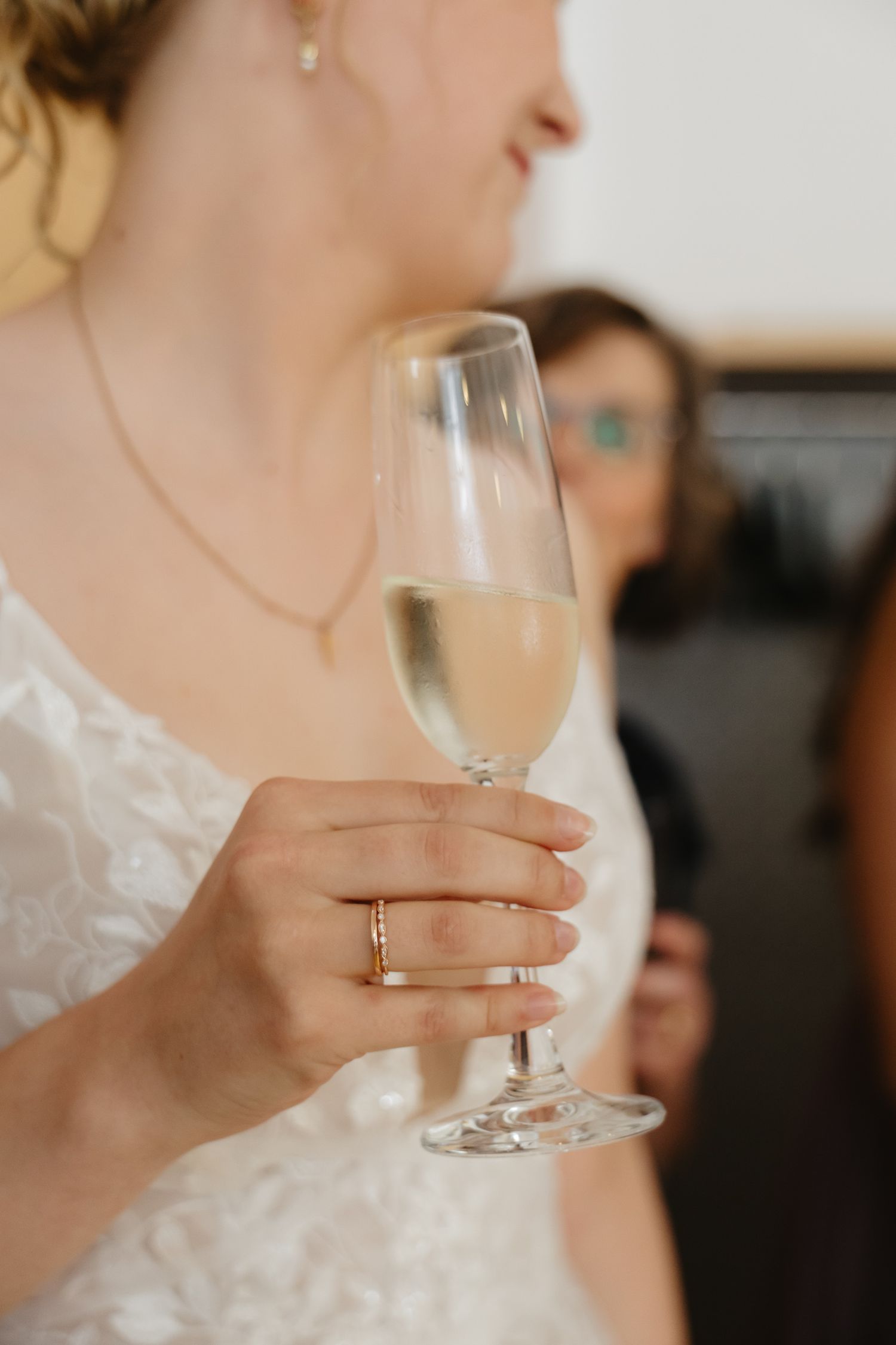 Close-up shot of hands holding a champagne glass with a wedding ring visible.