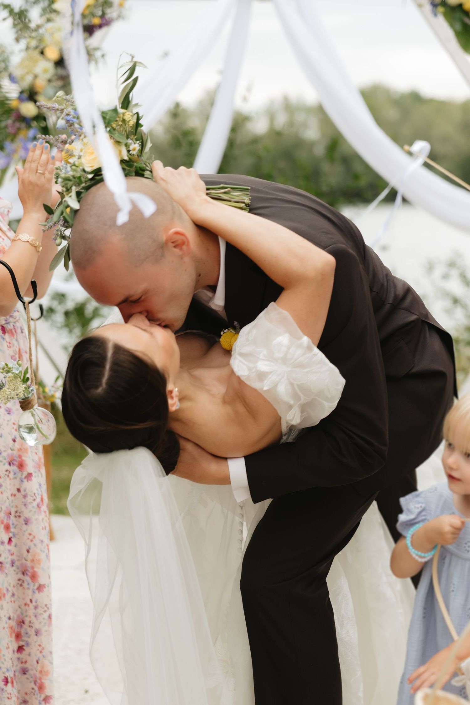 Romantic wedding ceremony kiss under a white draped arch with floral accents.