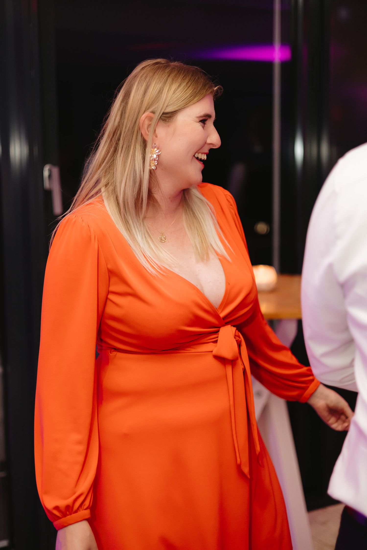 A person in a bright orange dress with puff sleeves is shown smiling and looking to the side.