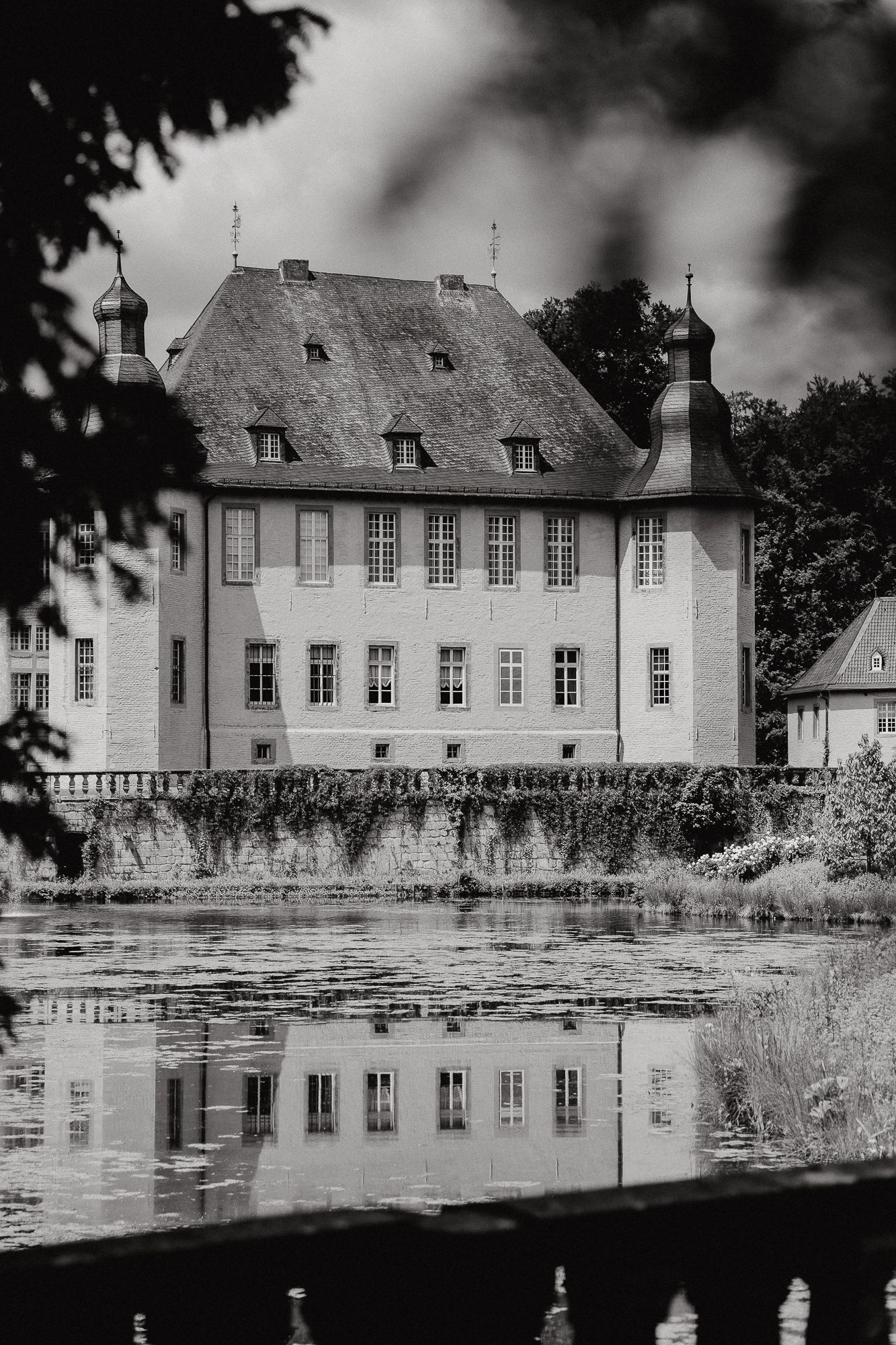 Black and white photograph of a stately manor house reflecting in a serene pond.