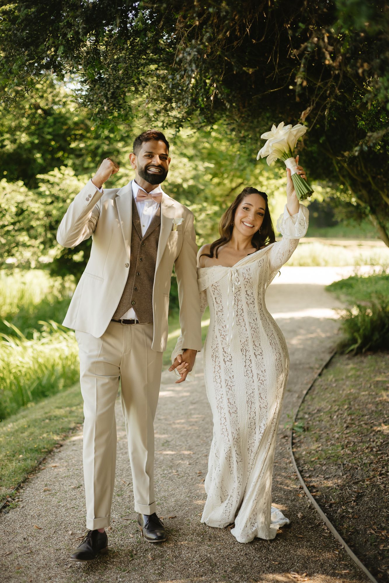 Romantic couple walking and dancing together on a garden path in wedding attire.