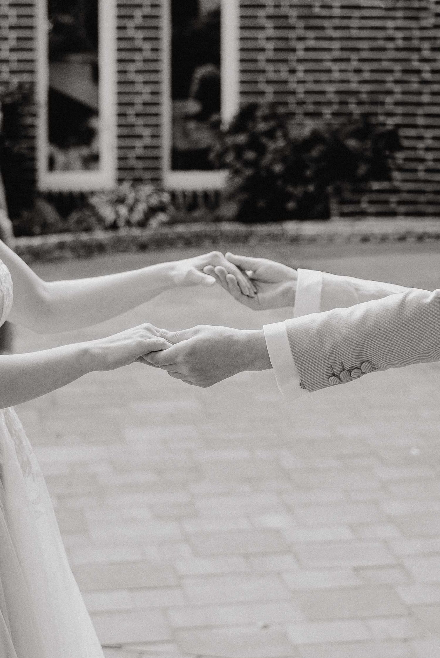 Two hands reach out and touch fingertips against a brick building backdrop in a graceful, artistic pose.
