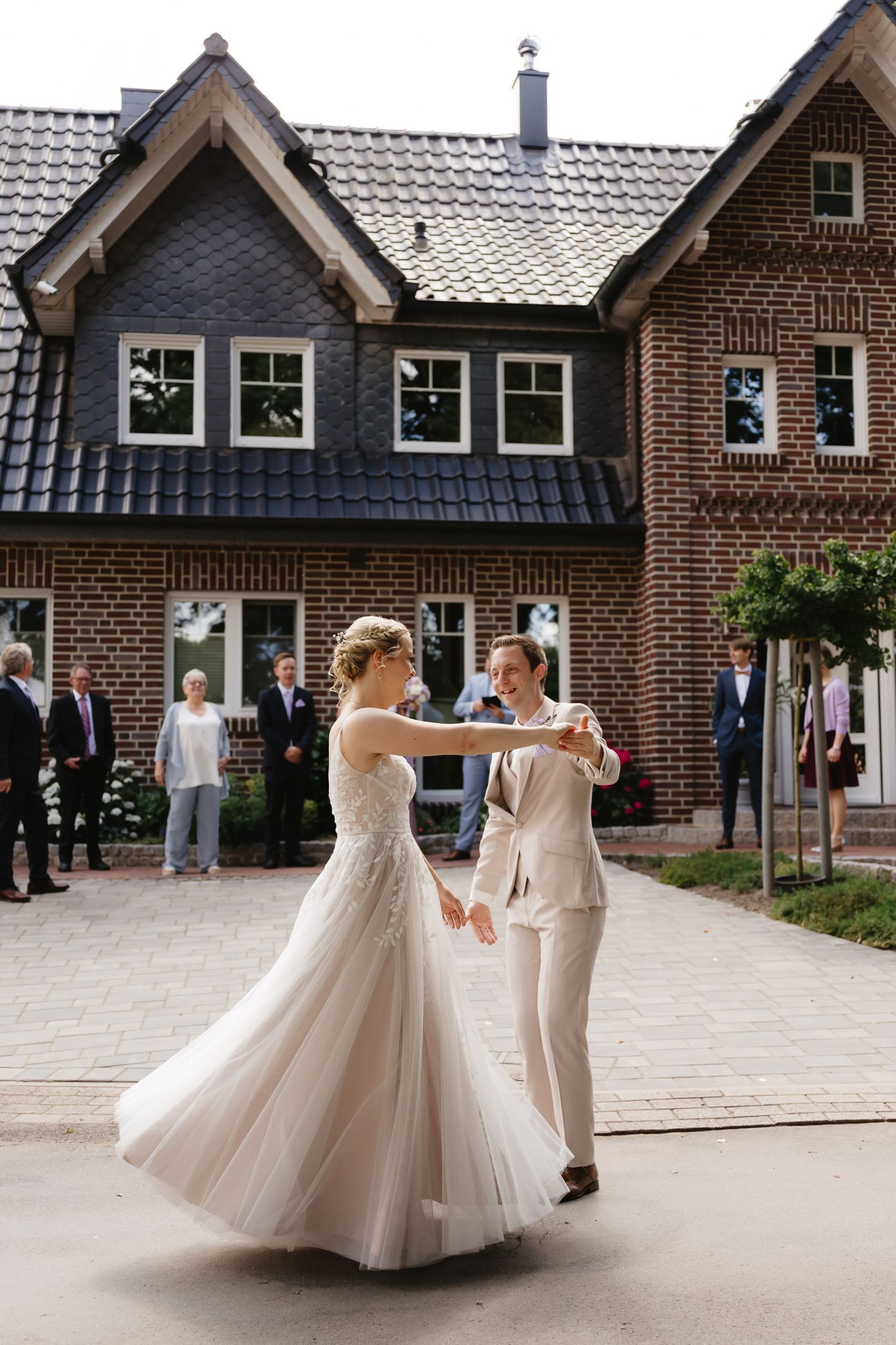 A couple dances together in a romantic twirl, with the bride wearing a flowing tulle gown outside a brick building.