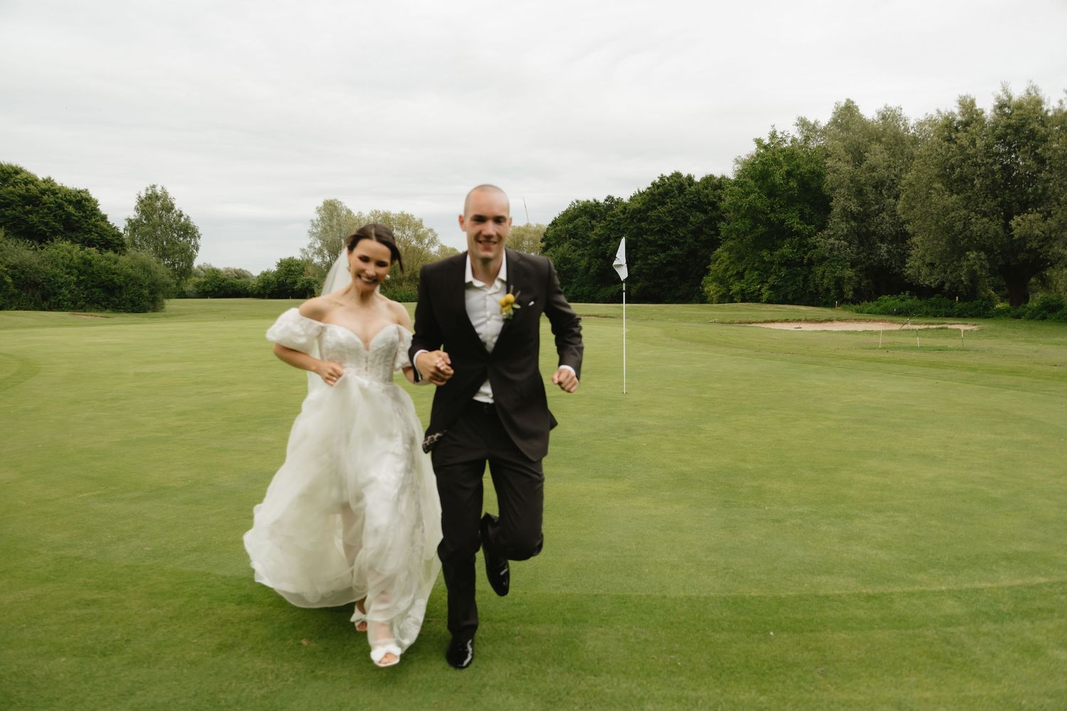 Newlyweds running playfully across a green lawn after their ceremony.