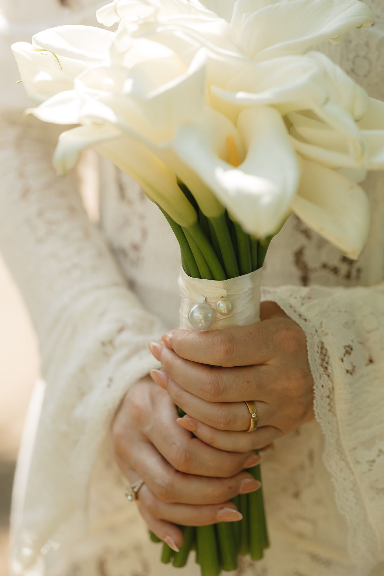 Elegant white calla lily bouquet held against a lace wedding dress.