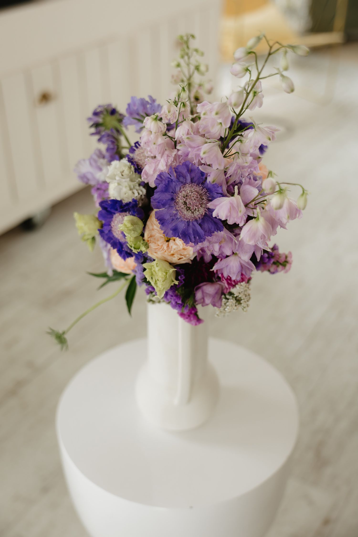A series of delicate purple and pink floral arrangements displayed in white vases on a light surface.