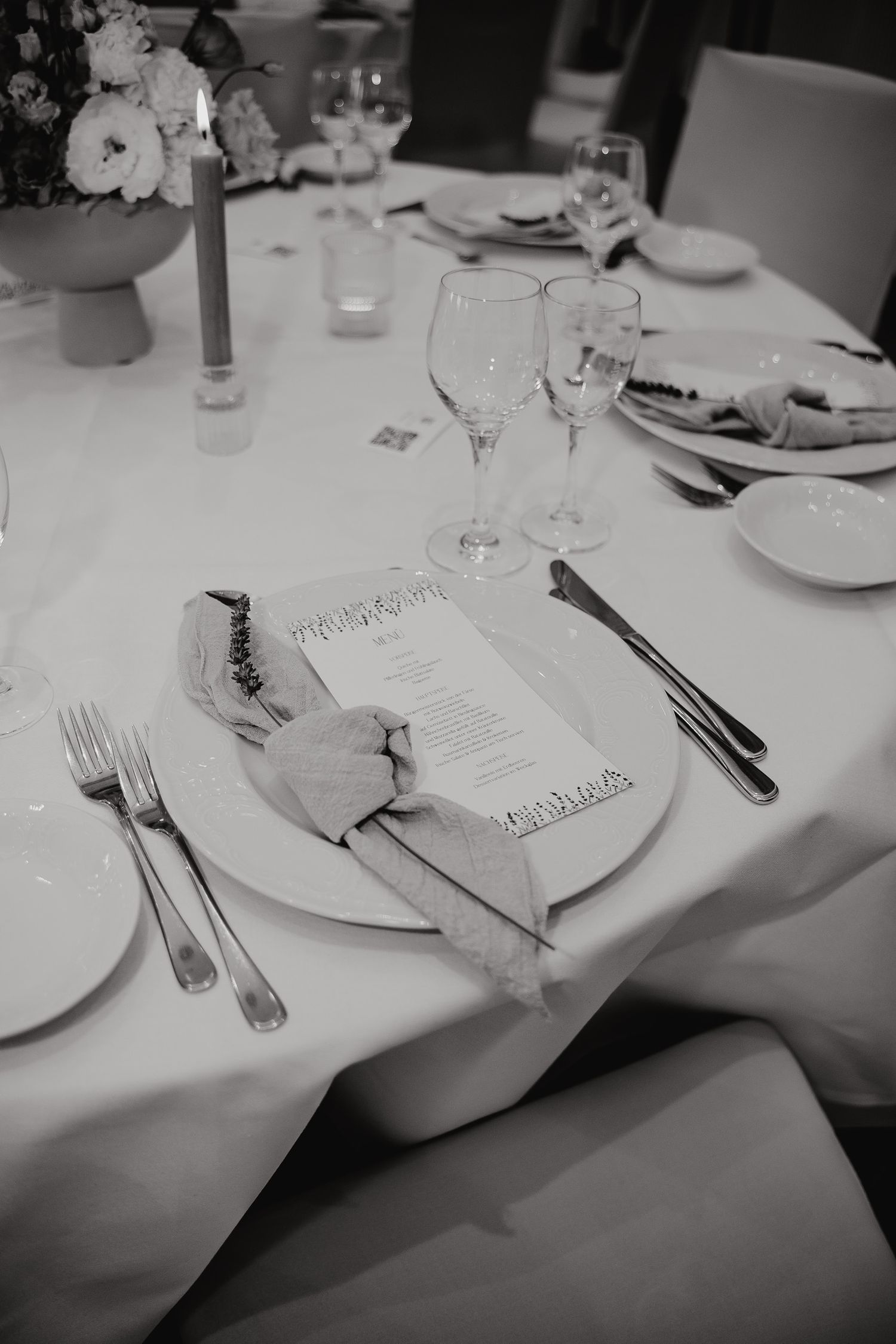 Black and white image of elegant table settings with white plates and wine glasses on crisp tablecloths.