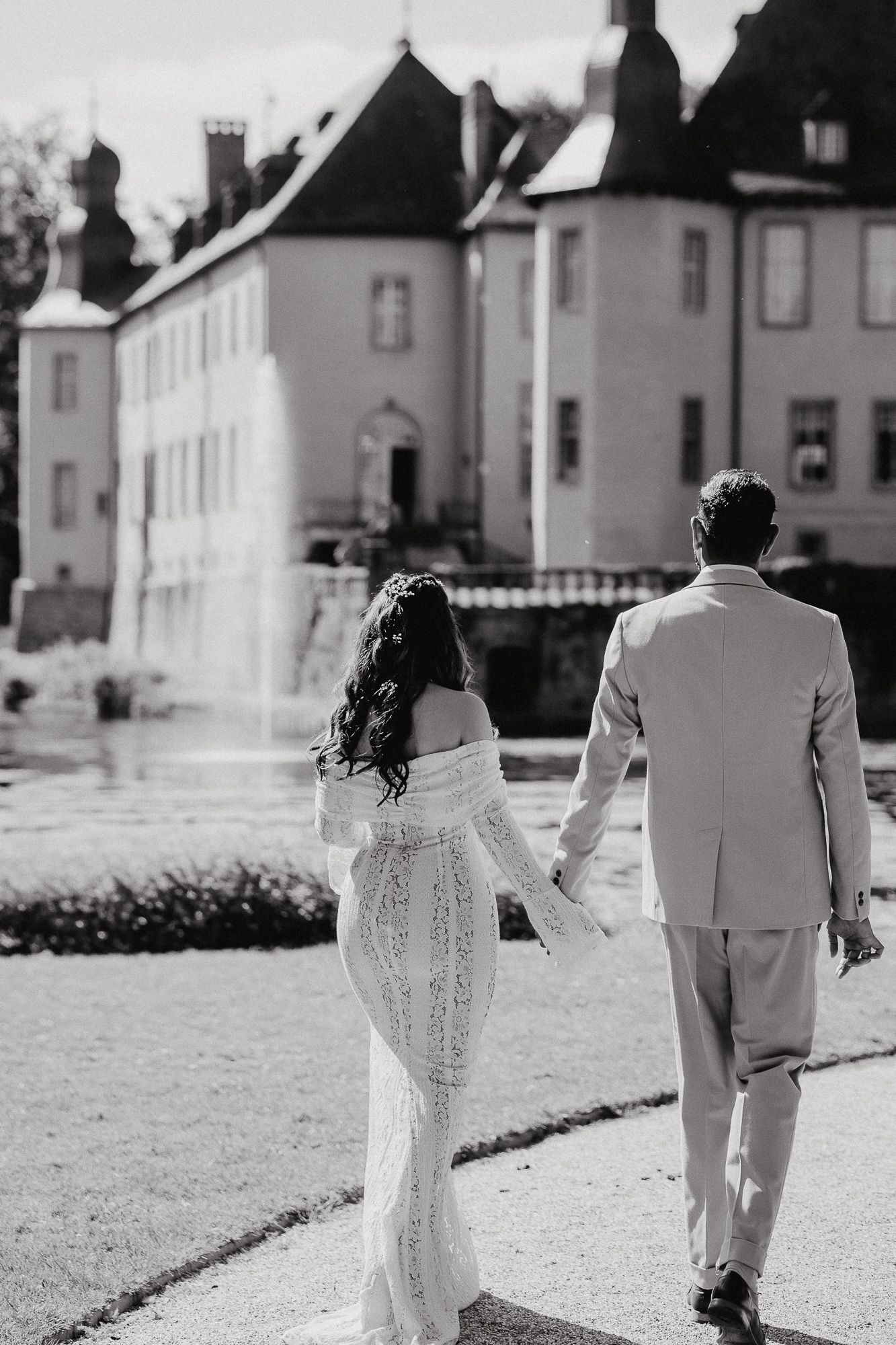 Black and white wedding photo of couple walking away from historic buildings.
