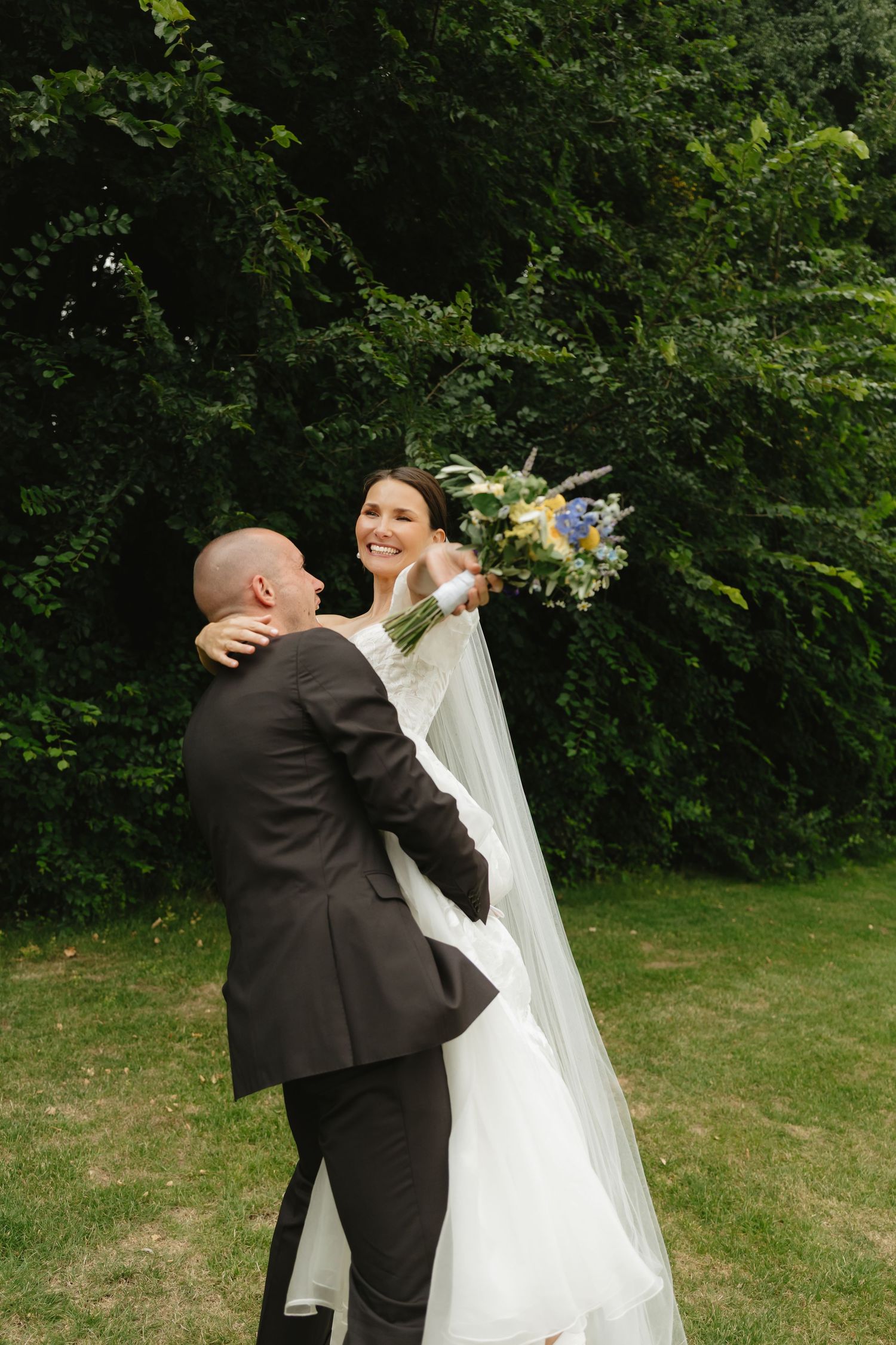 Joyful wedding couple dancing and twirling in a green garden setting.