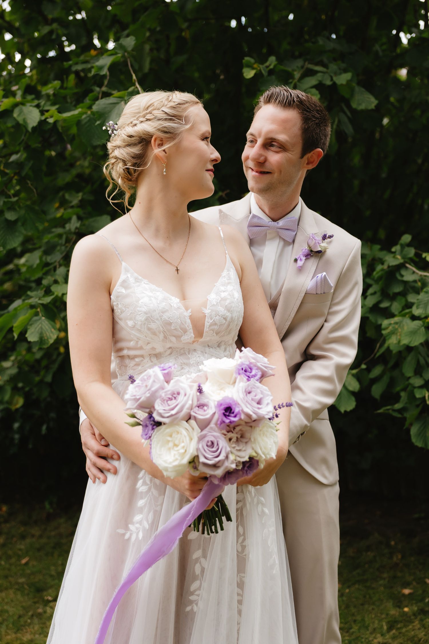 A romantic wedding moment in a garden setting with a beautiful white gown and purple floral bouquet.