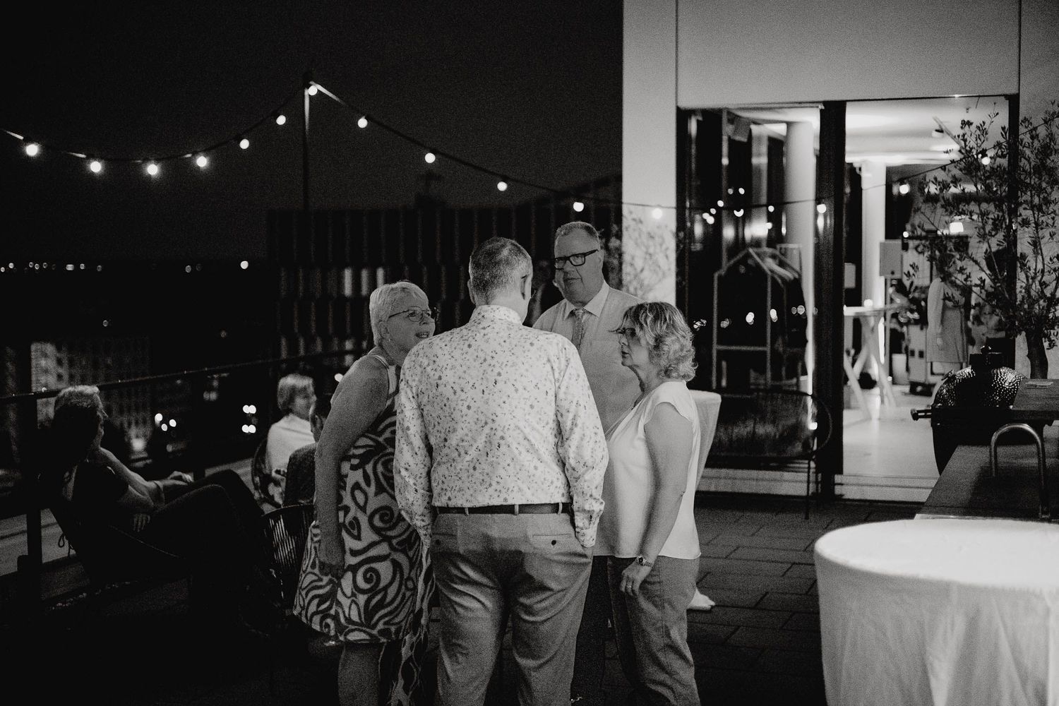 String lights illuminate an outdoor evening wedding reception with guests mingling and dancing at dusk.