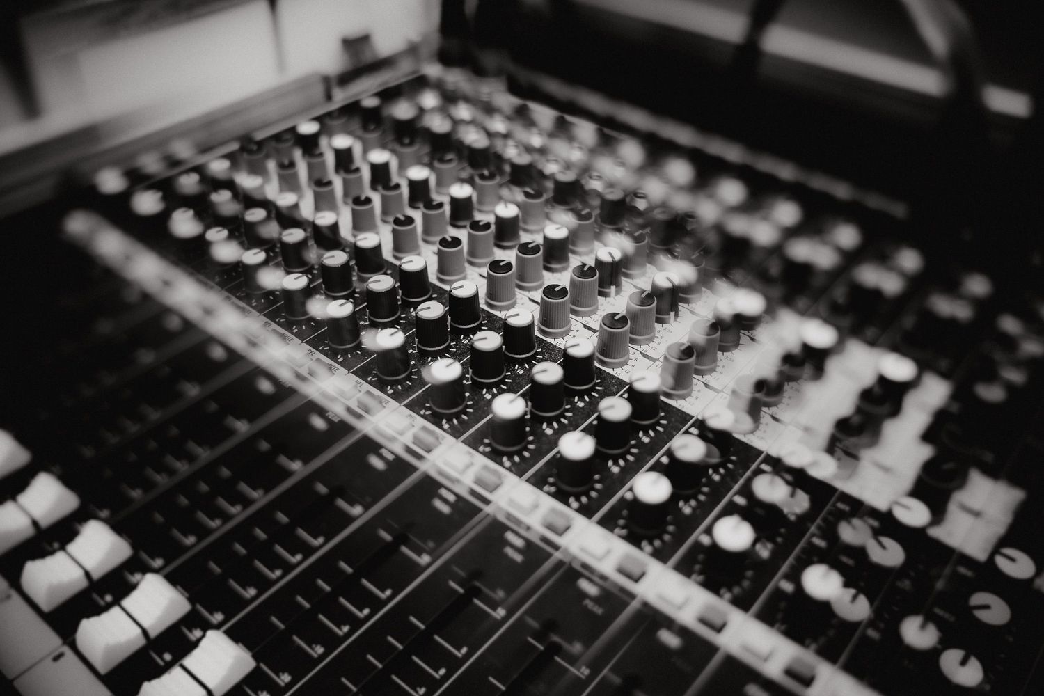 Close-up view of a professional audio mixing console with multiple faders, knobs and buttons in black and silver.