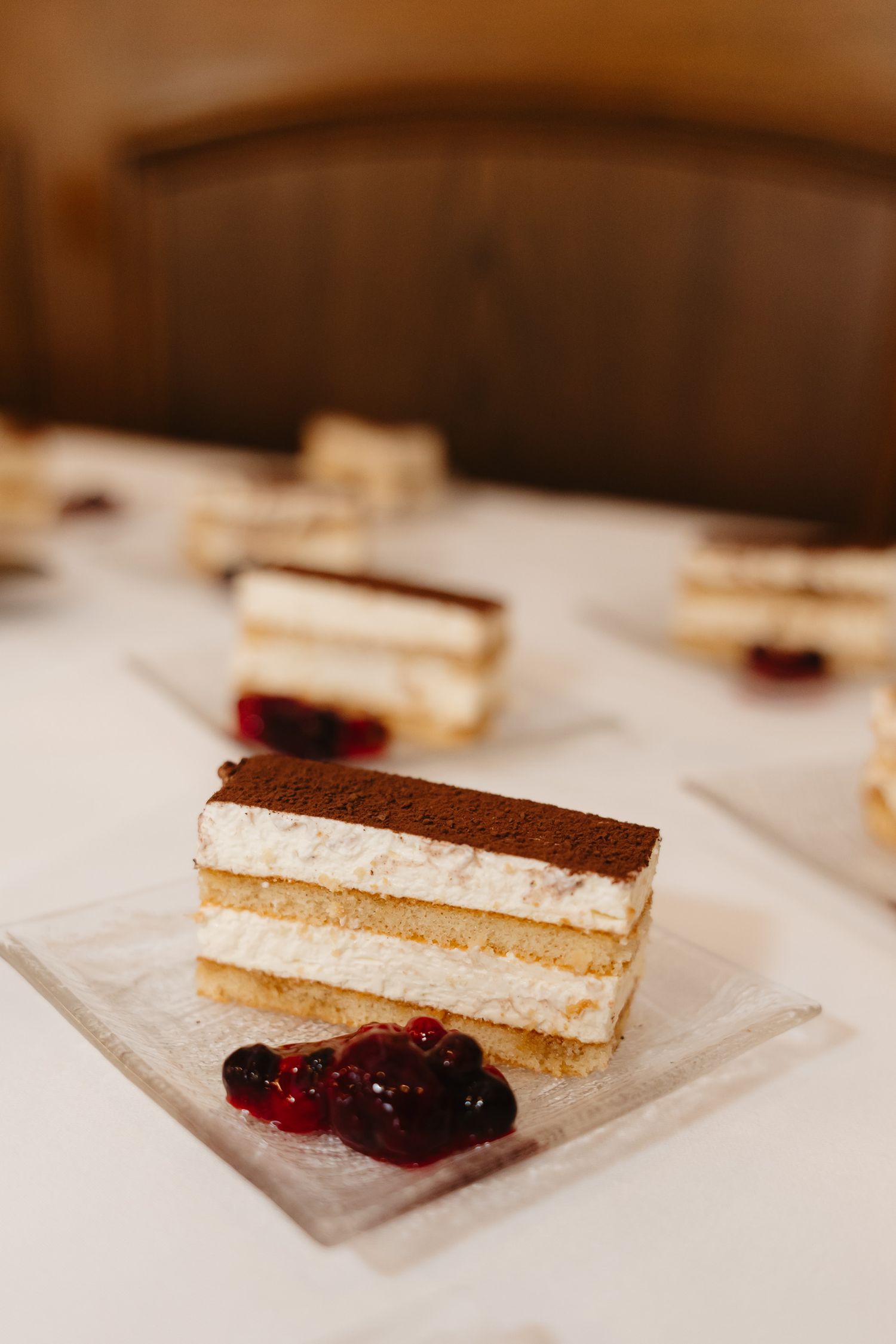 A slice of tiramisu cake with layers of cream and cocoa powder, served with dark berries on a white plate.