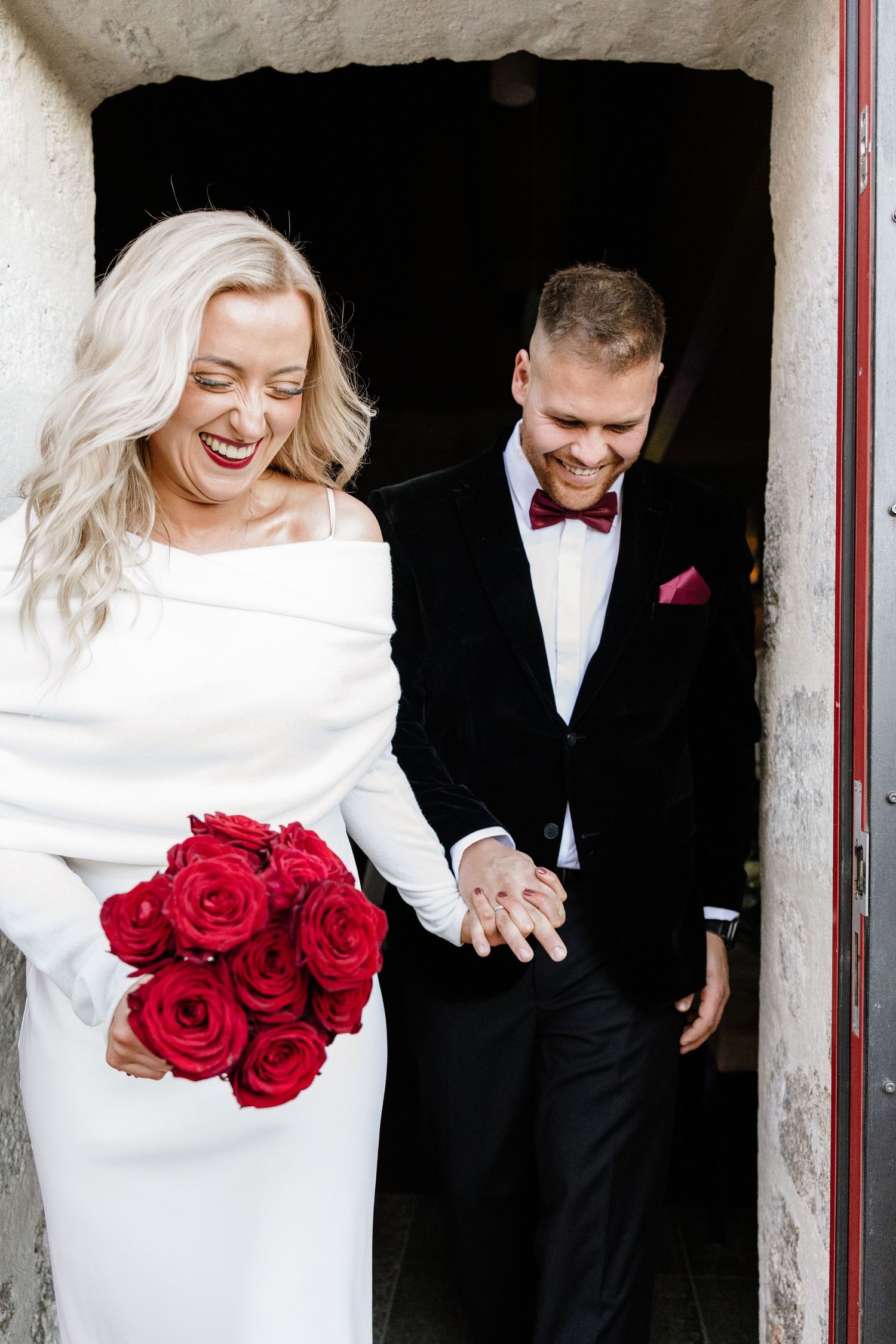 Elegant winter wedding scene with red roses and off-shoulder white dress.