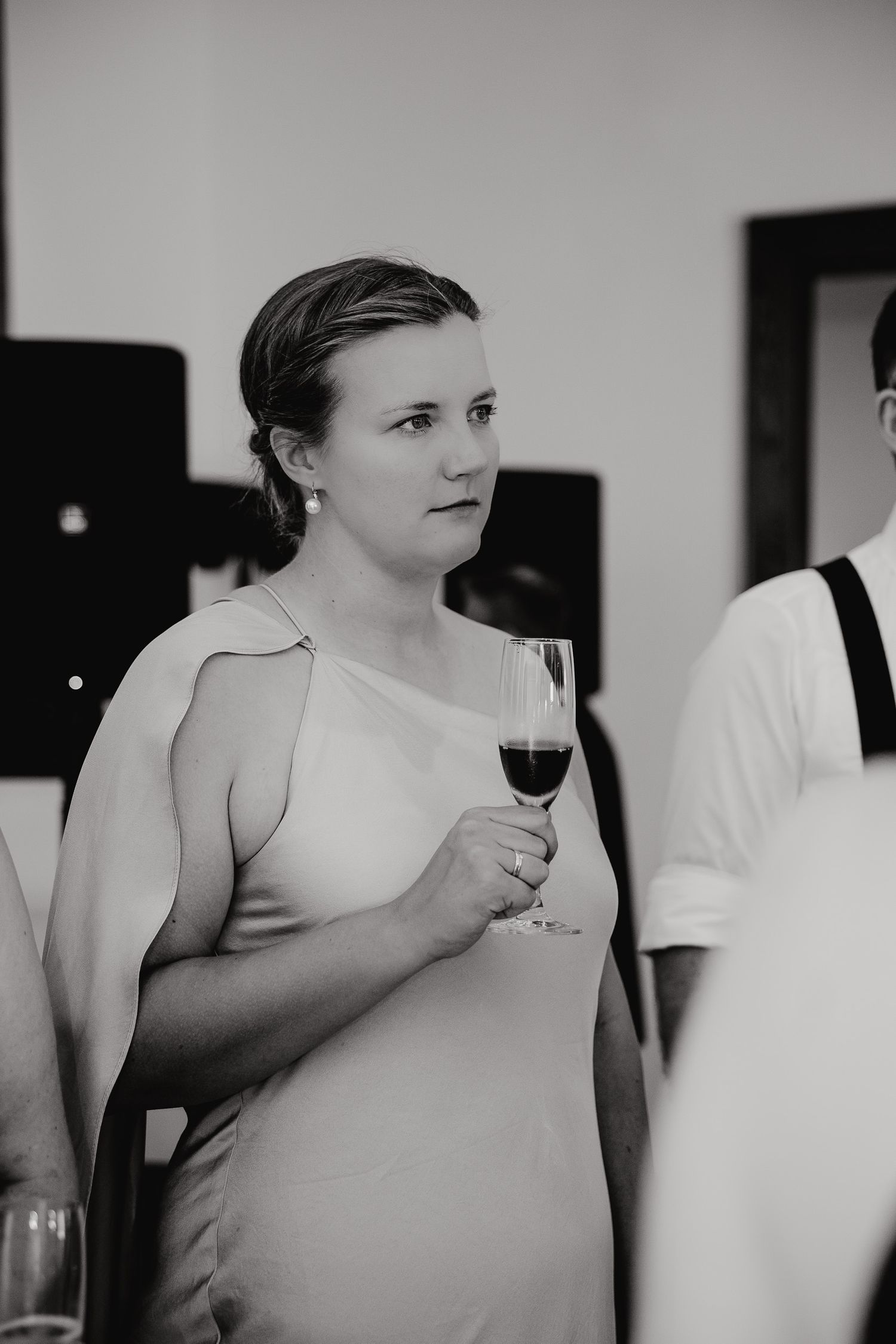 A person in a sleeveless white top holds a glass of red wine while attending a social gathering.