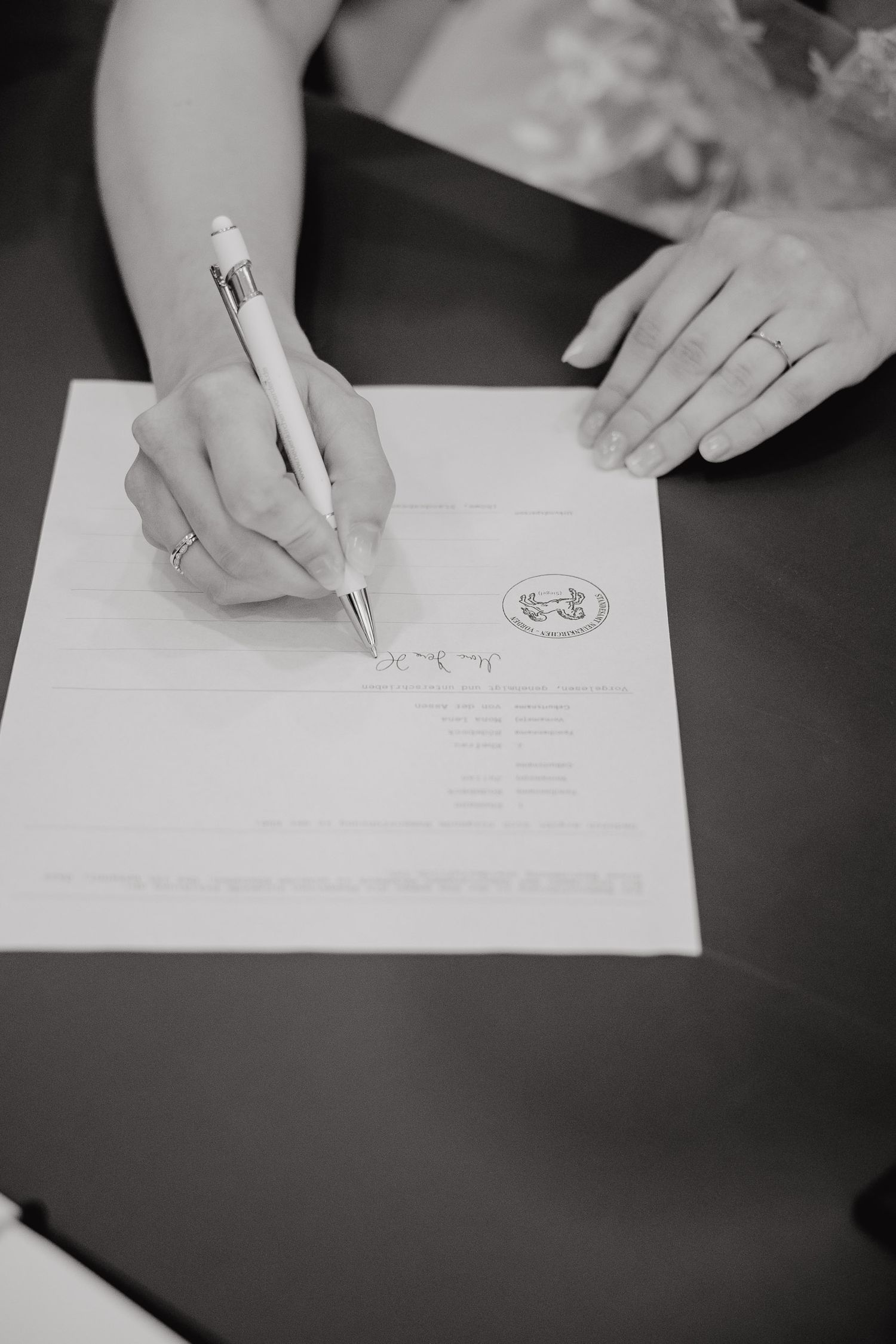 Black and white close-up images of hands signing official documents with pens on a dark surface.