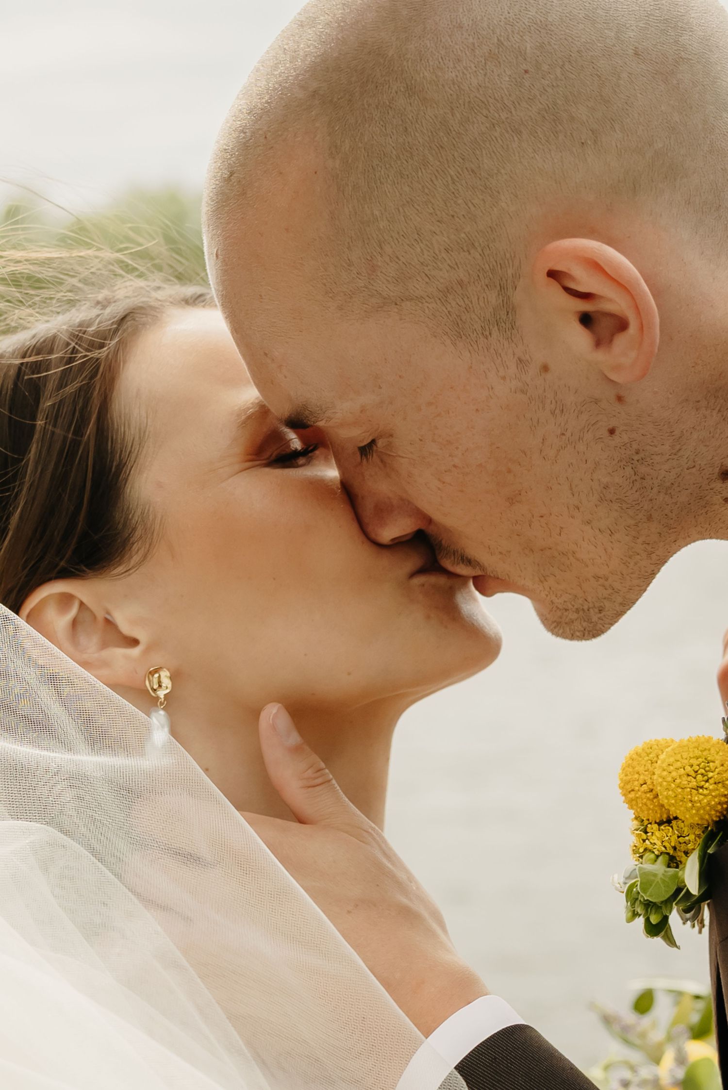 Close-up profile of a tender wedding kiss with a yellow flower in the foreground.