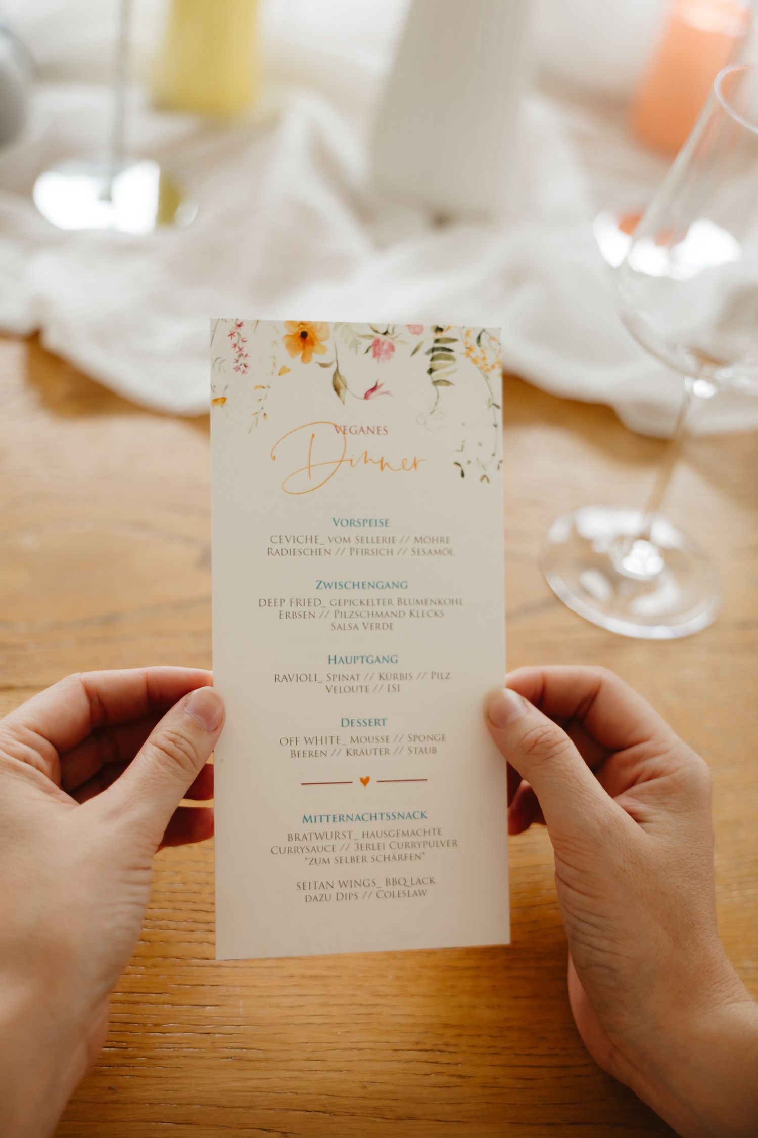 A series of wedding menu cards being held and displayed on a wooden table with glassware in the background.