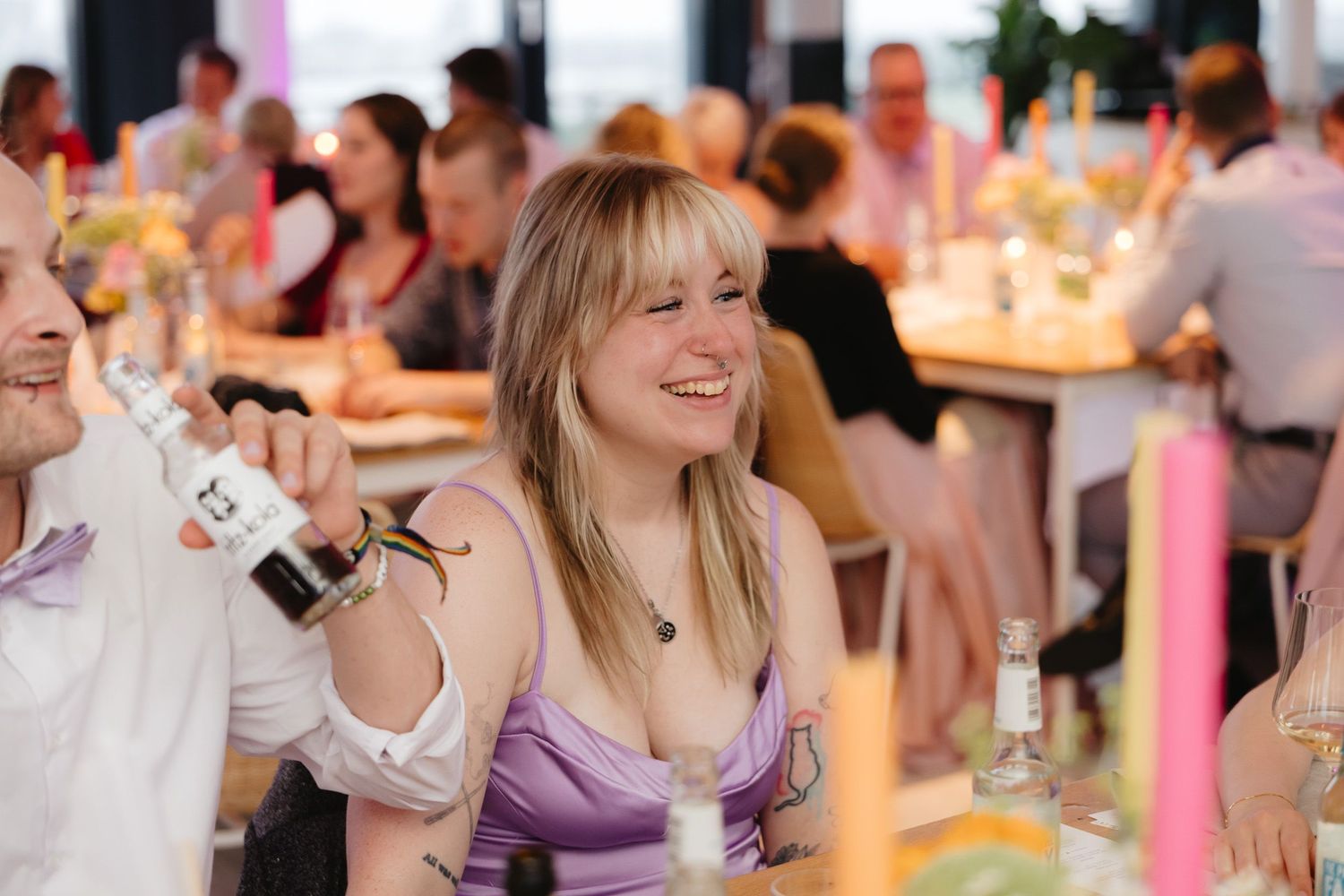 Wedding guests dance and celebrate at a reception with colorful lighting and festive atmosphere.