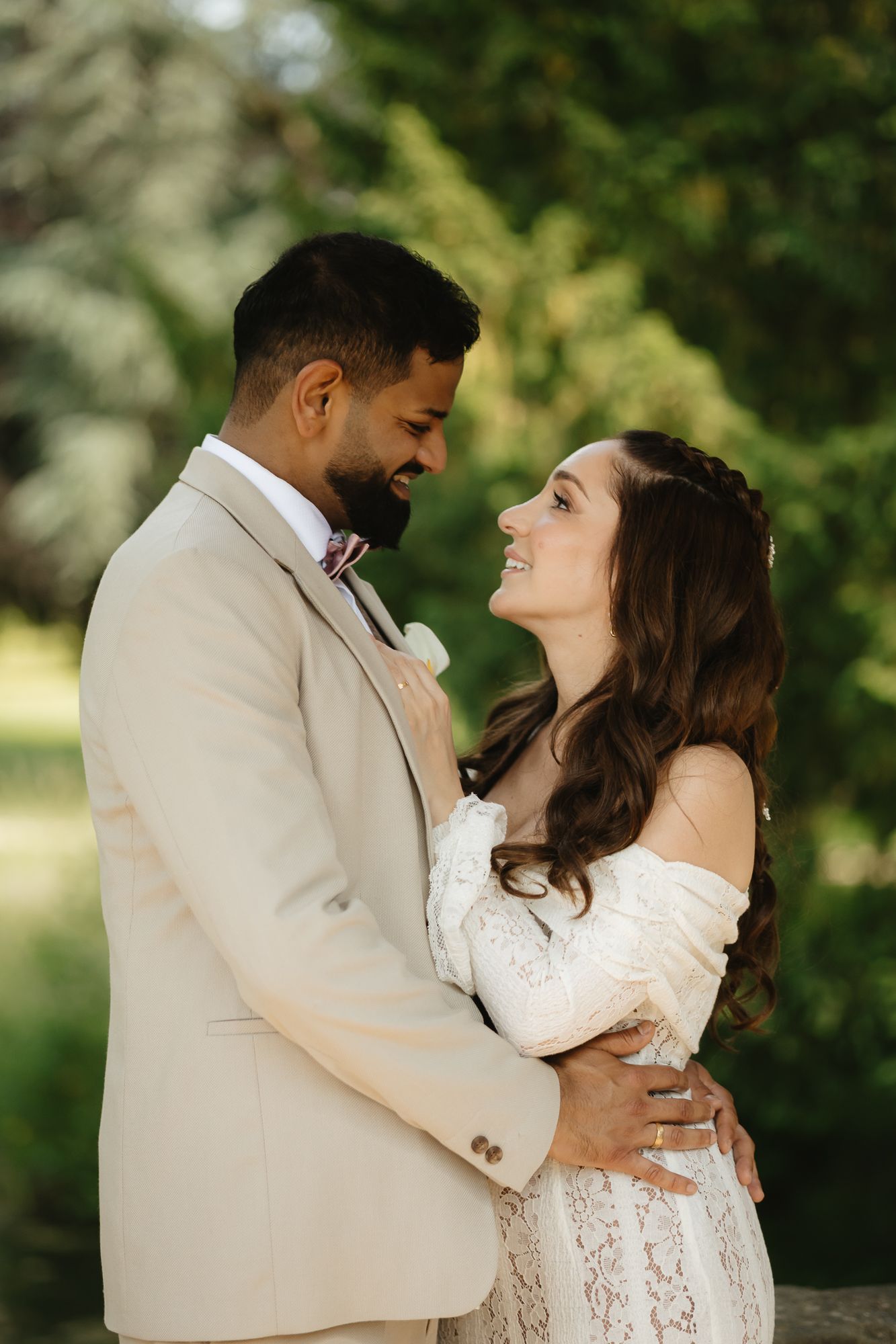 Romantic wedding couple embraces outdoors in natural lighting with lace dress and light colored suit.