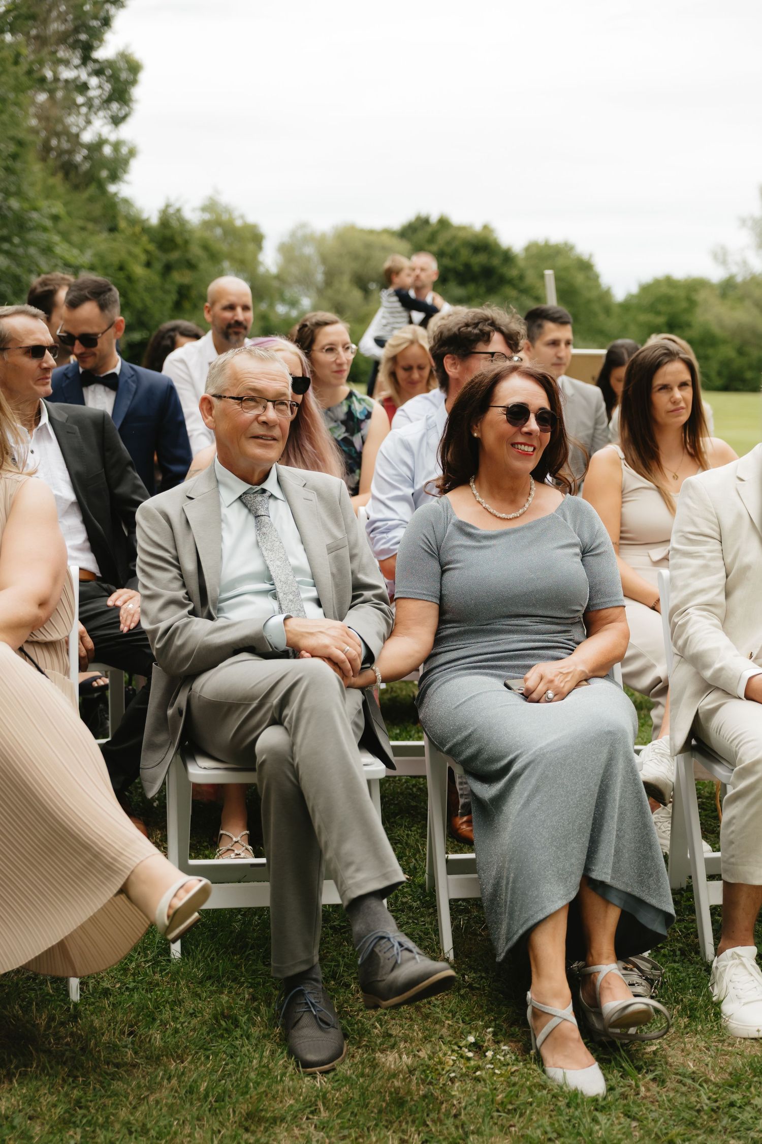 Wedding guests seated outdoors in formal attire enjoying the ceremony.