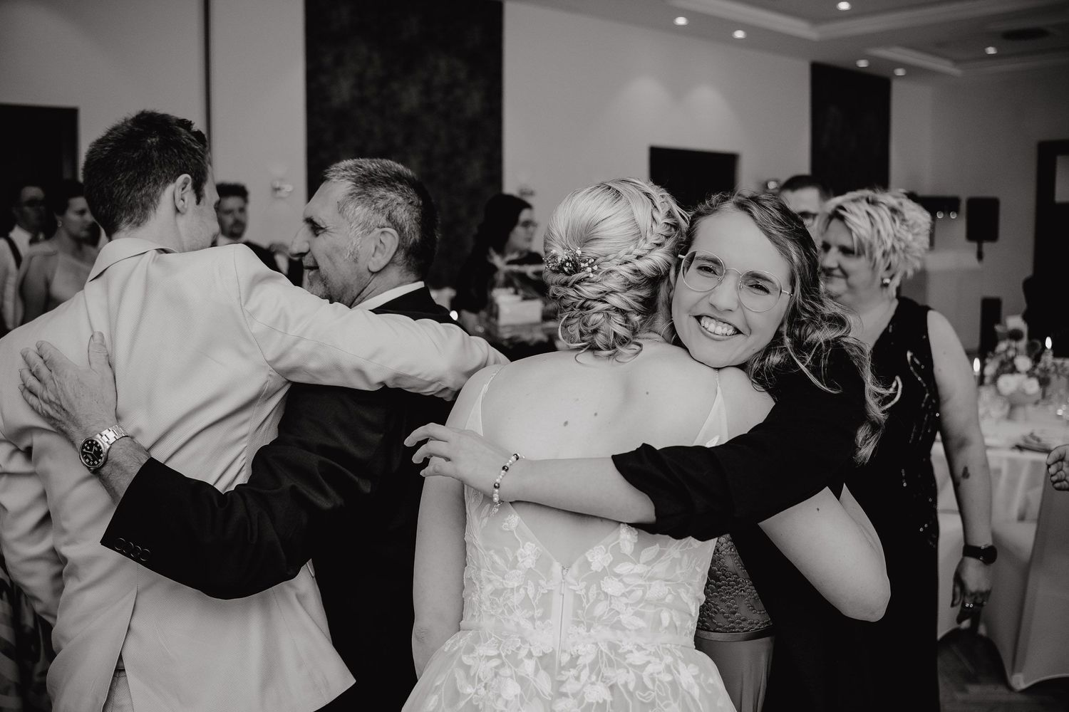 Black and white photo of people embracing and dancing at a wedding reception celebration.