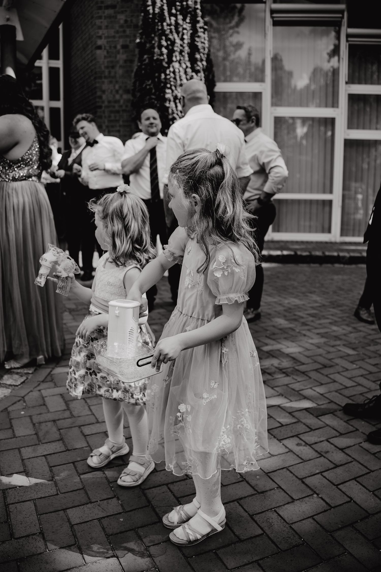 Young children in formal attire dance together on a brick patio during a wedding celebration.