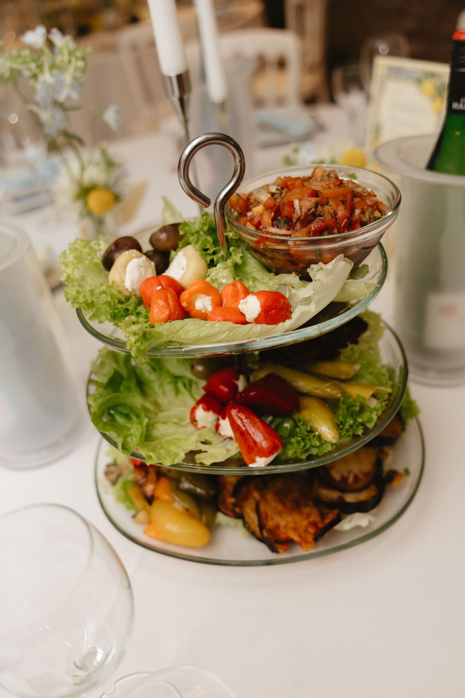 Tiered serving platters with fresh salads and appetizers on white tablecloths.