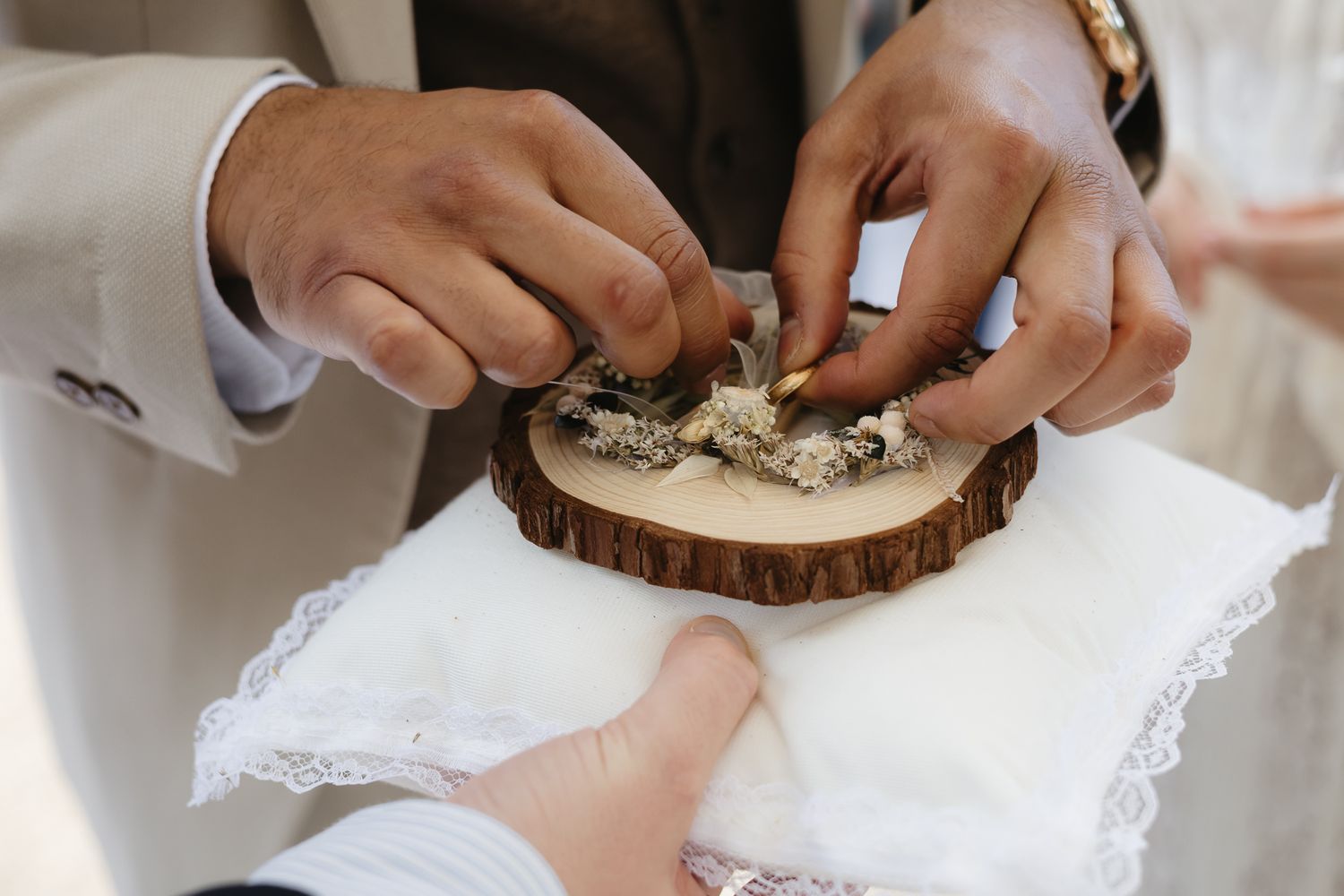 Close-up of hands exchanging rings during wedding ceremony on rustic wooden surface.