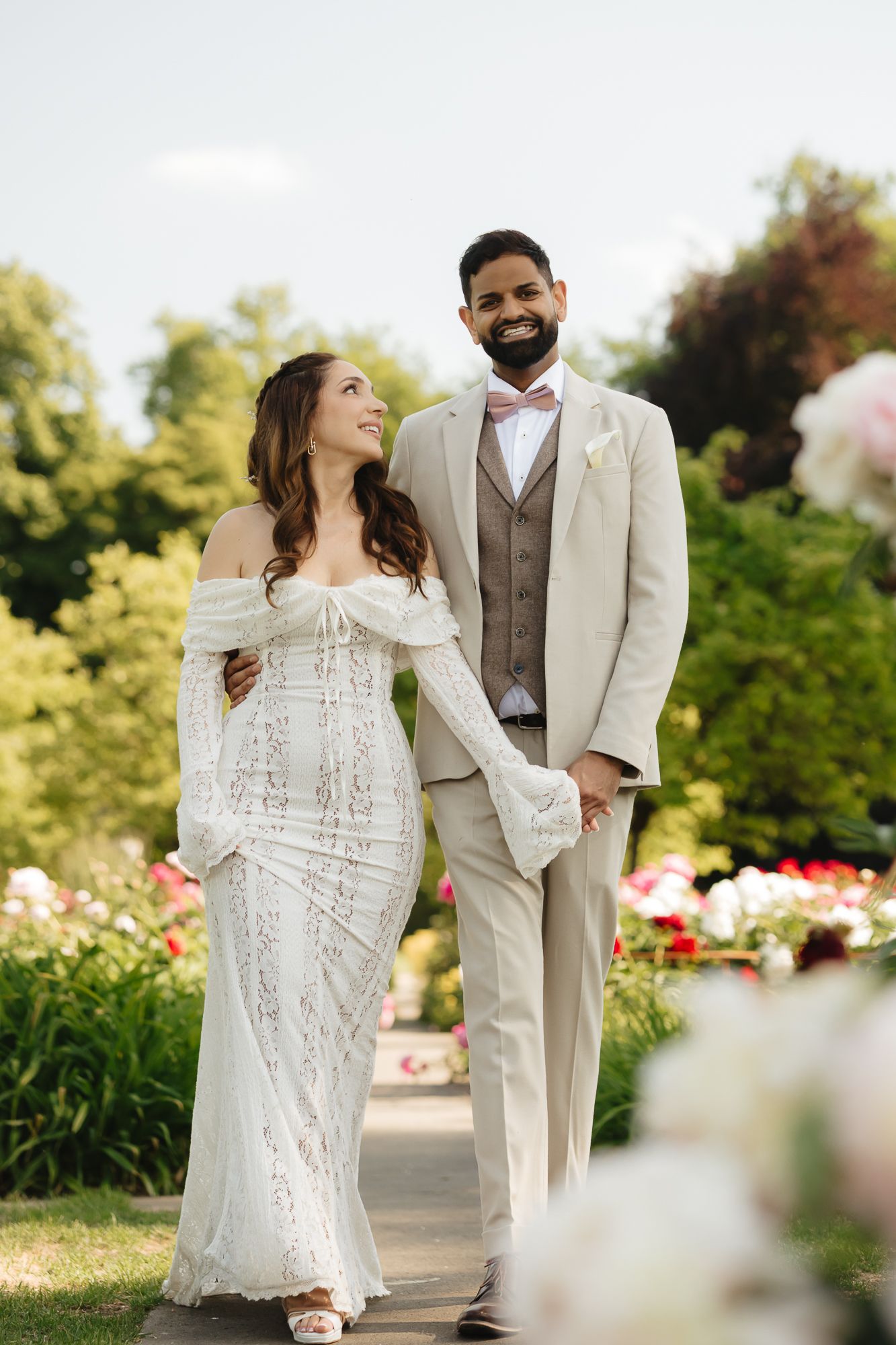 Romantic couple in wedding attire posing in a garden with blooming flowers.
