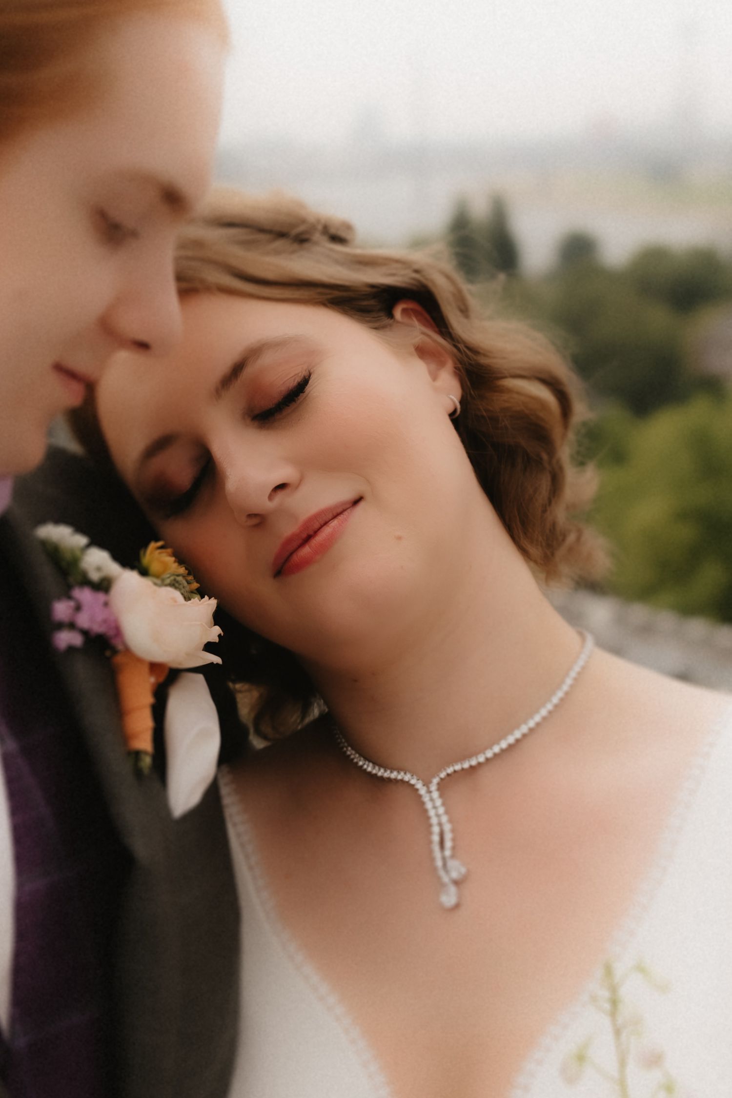 A bride wearing a pearl necklace poses in a romantic outdoor setting with soft lighting and floral accents.