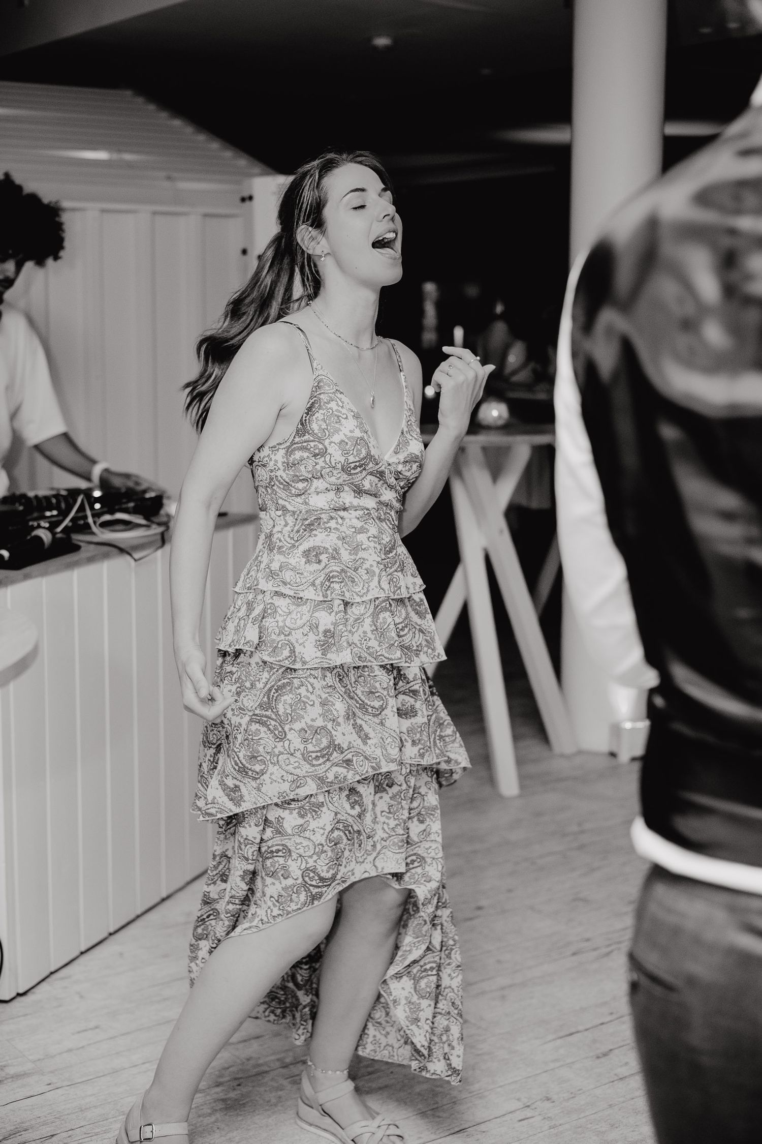 A person in a floral dress dances energetically on a dance floor during what appears to be a celebration.