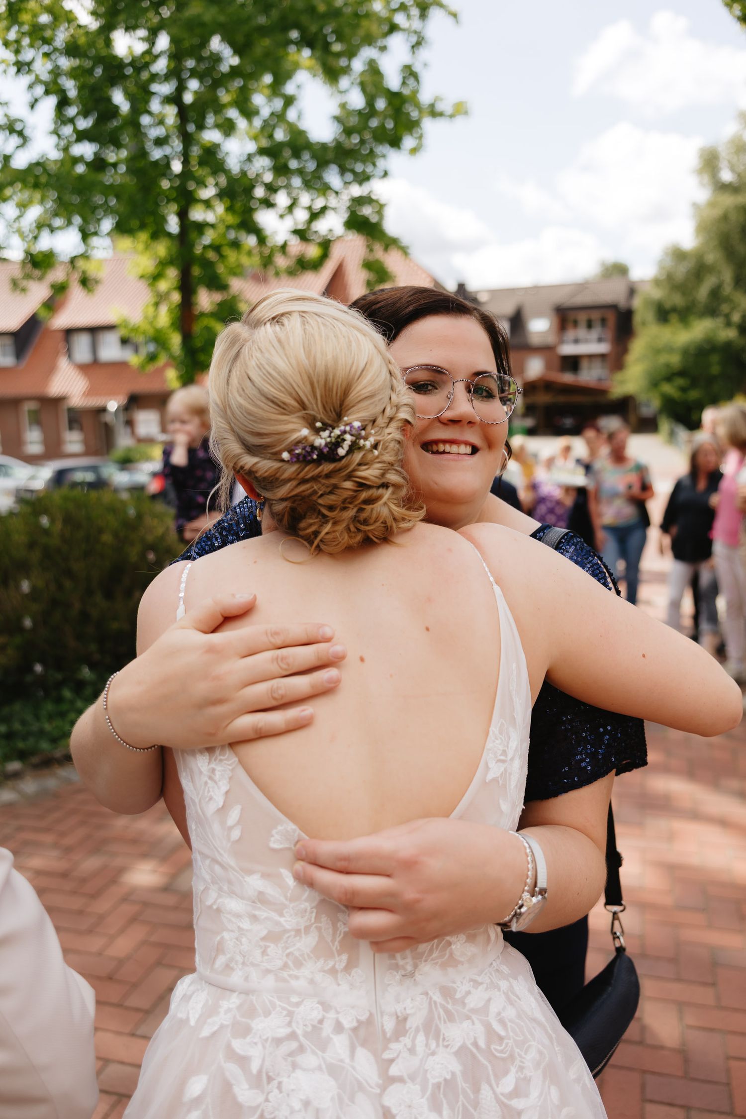 A sequence of joyful hugs between wedding guests on a brick patio during an outdoor celebration.