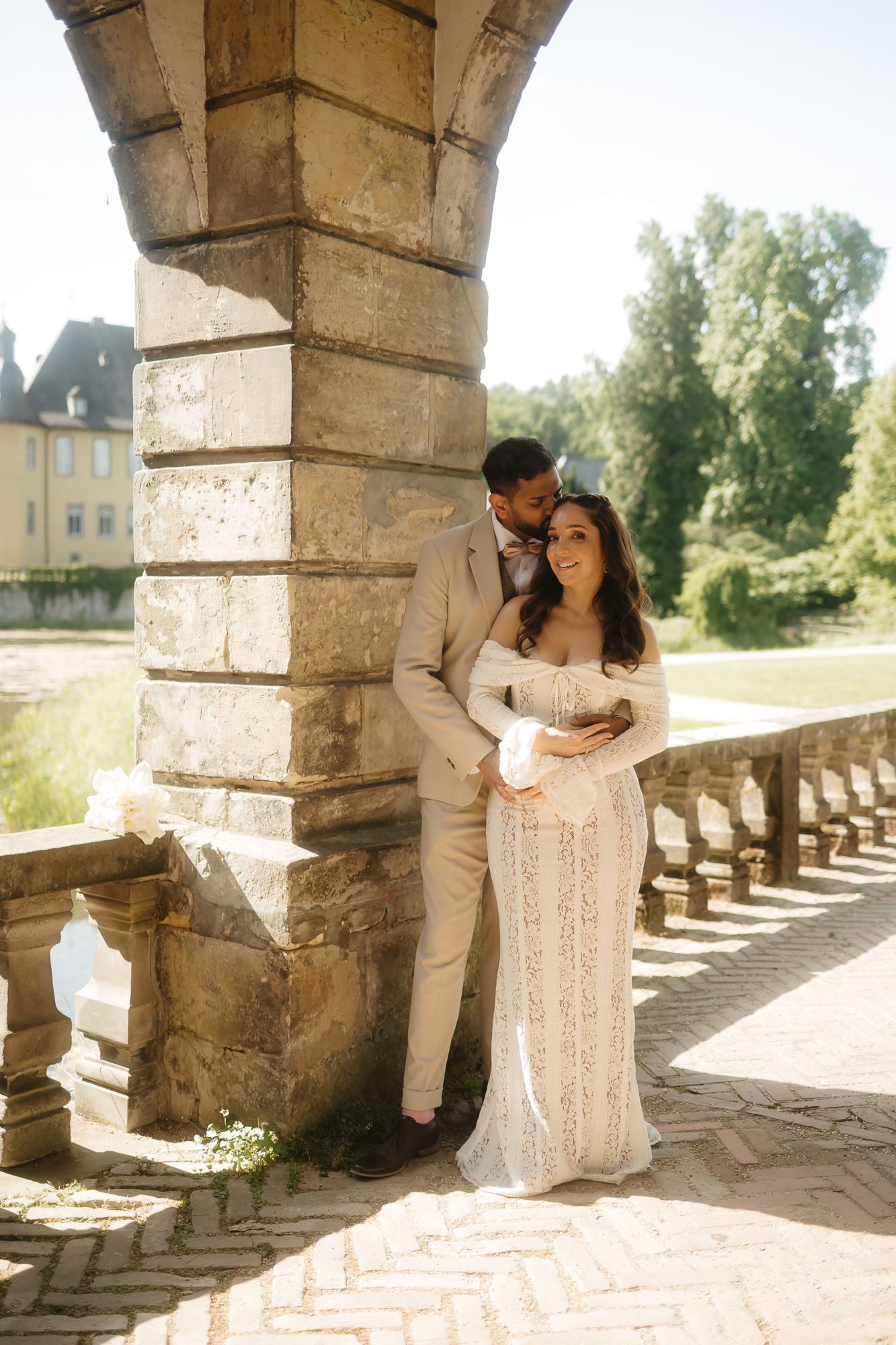 Romantic wedding portraits under stone archway with sunlit garden backdrop.