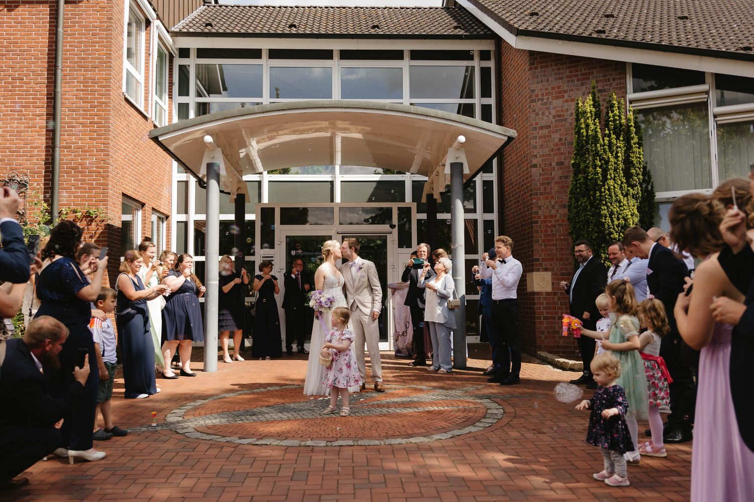 Wedding guests line up outside a brick building to celebrate during an outdoor reception ceremony.