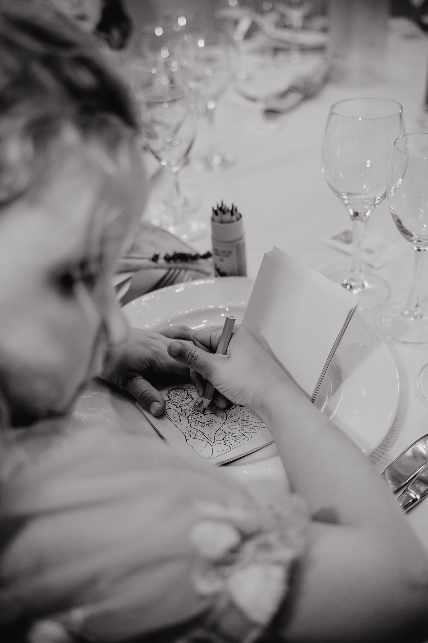 Close-up shots of hands writing on paper at an elegant table setting with wine glasses and white tablecloths.