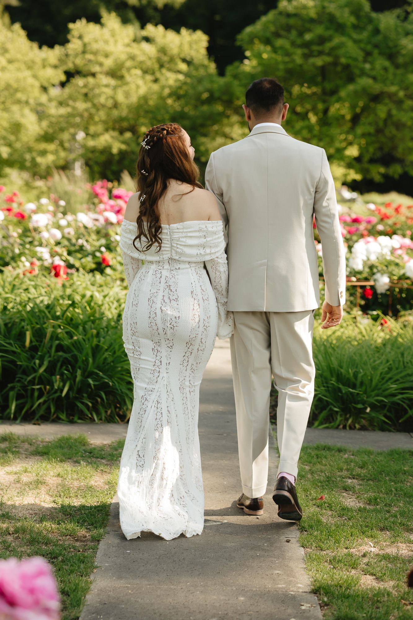 Couple walking along garden path surrounded by summer flowers and greenery.