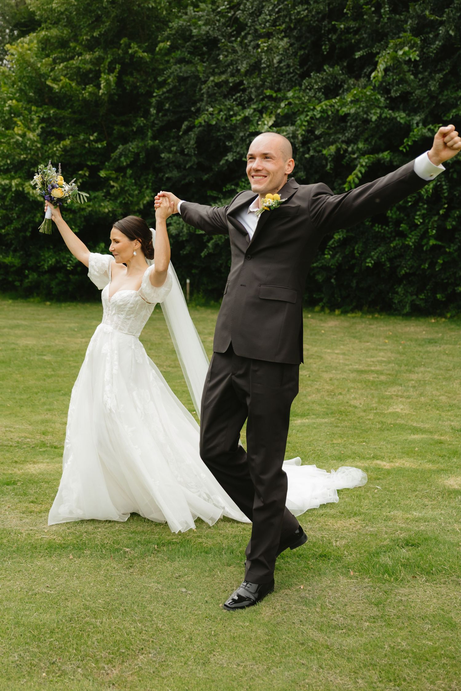 Newlyweds dancing playfully on a grassy lawn during their wedding celebration.
