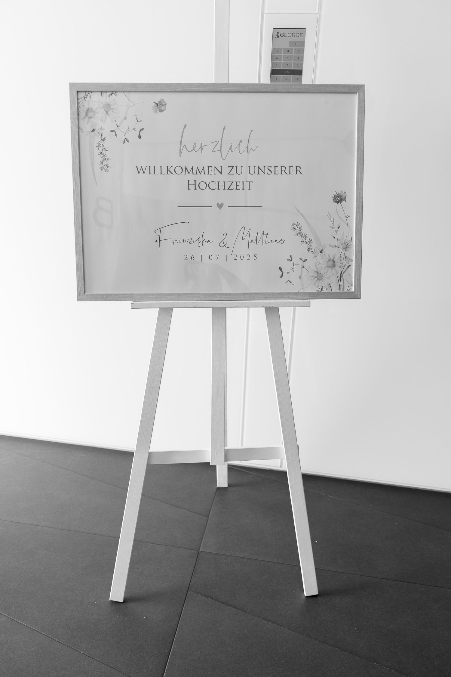 Four white easels displaying handwritten welcome signs stand against a light wall on dark flooring.