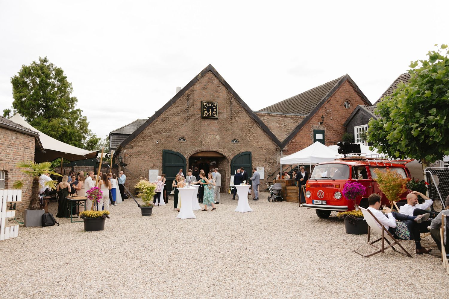 Panoramic view of a rustic brick venue exterior with guests gathered on a gravel courtyard.