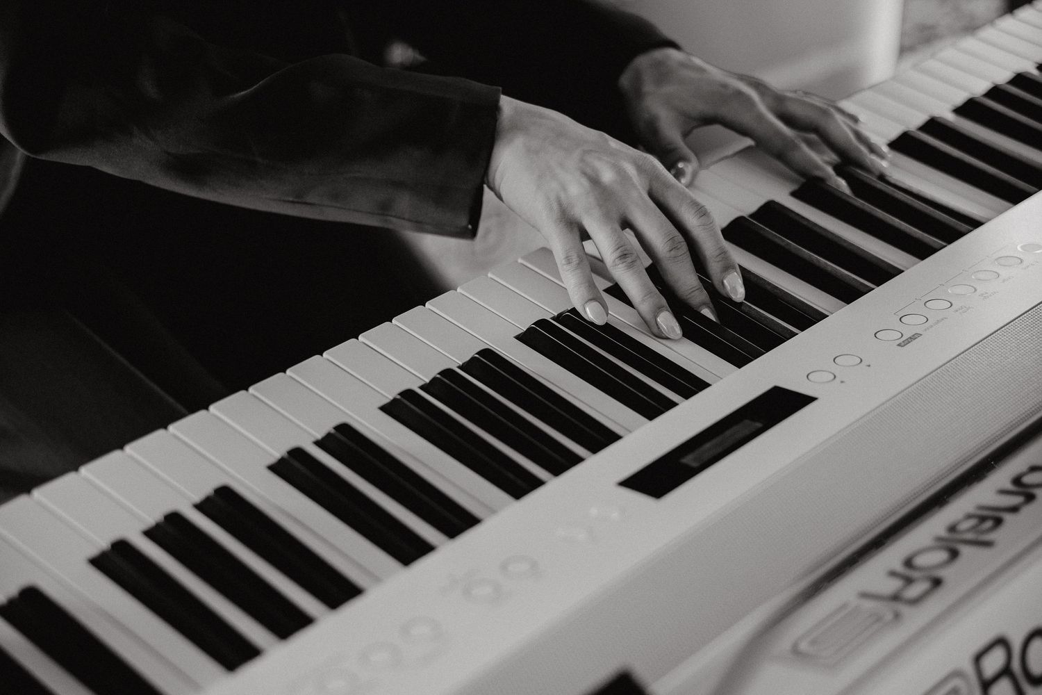 Hands playing on electronic keyboard keys in black and white.