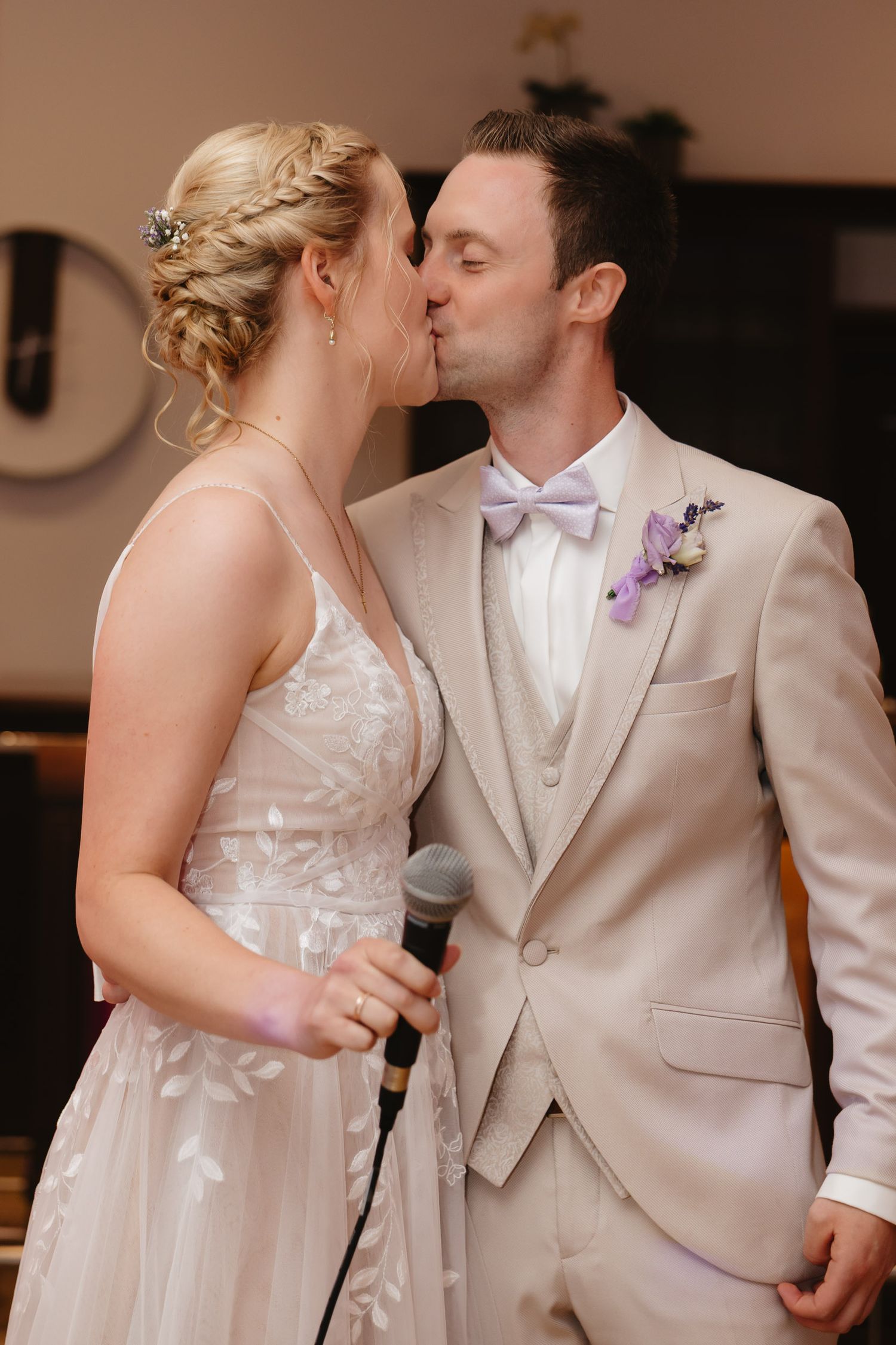 A bride and groom share a tender kiss during their wedding reception in a warm-toned indoor setting.